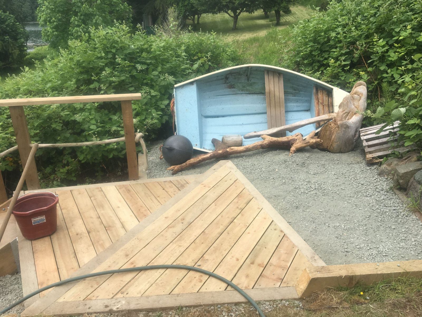 Finished cedar deck platform with timber railing beside a repurposed blue rowboat planter and shrubs