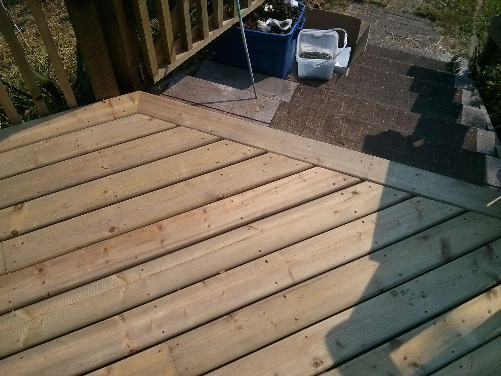 Close view of a newly built wood deck corner with angled boards meeting a shingled walkway