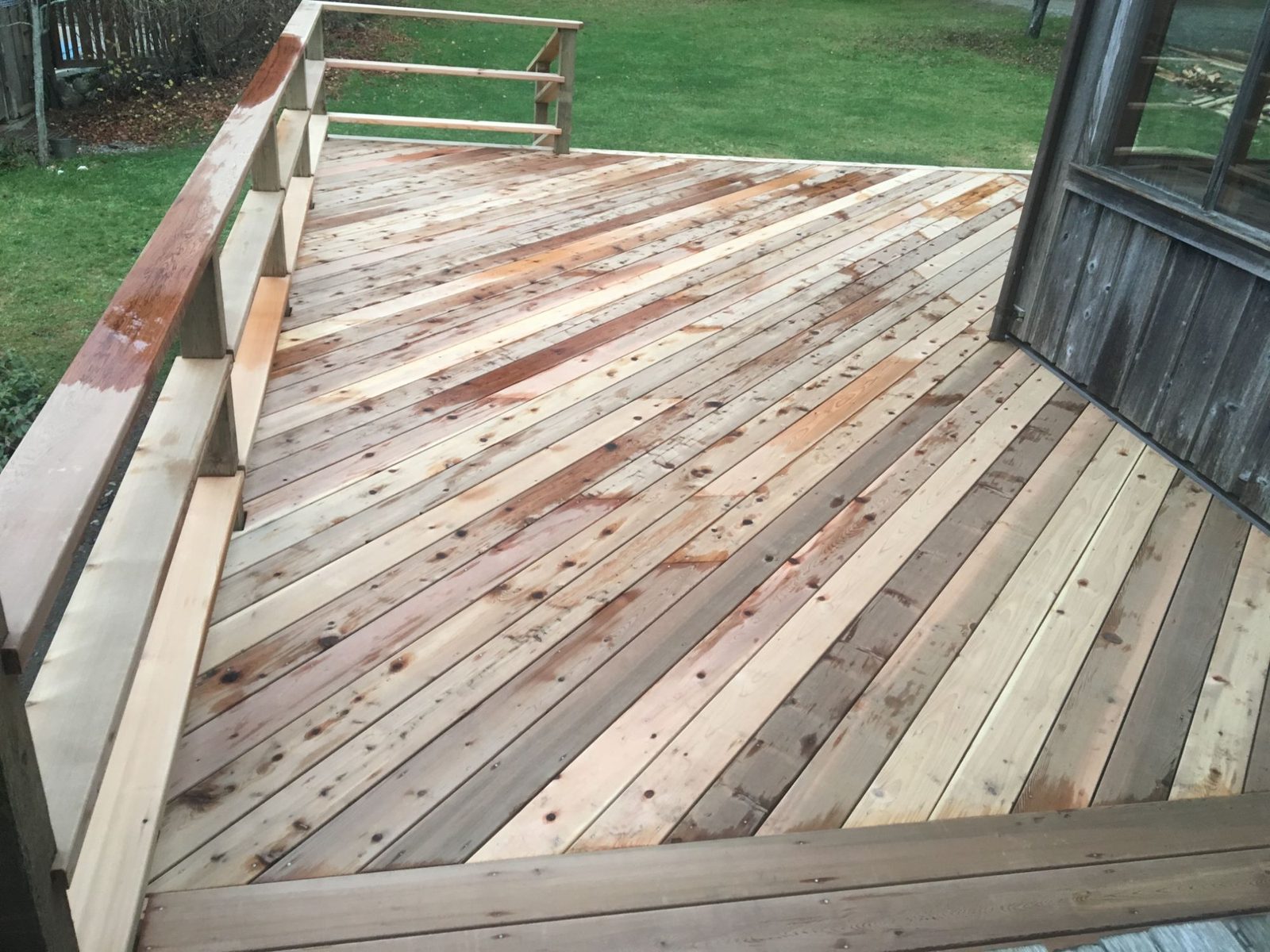 Cedar deck with mixed-tone boards, built-in bench and railing beside a weathered cabin and lawn