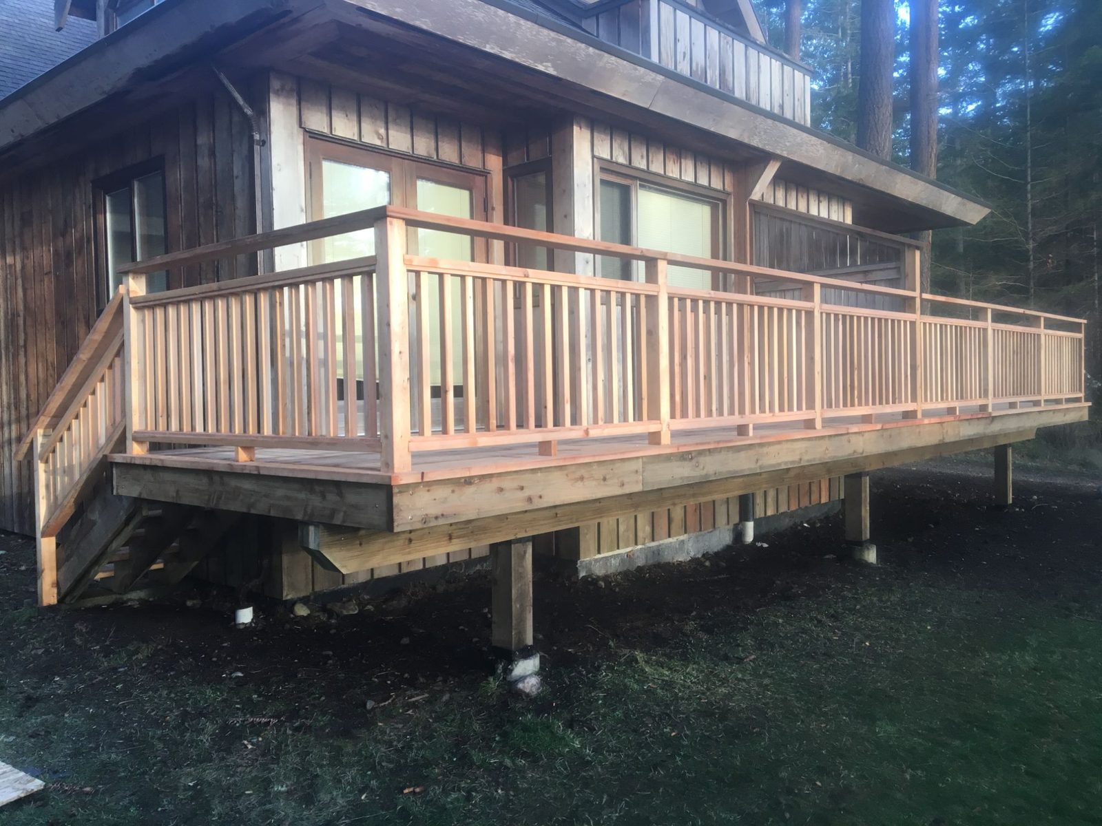 Raised cedar deck with full wood railing and side steps wrapping a forest cabin