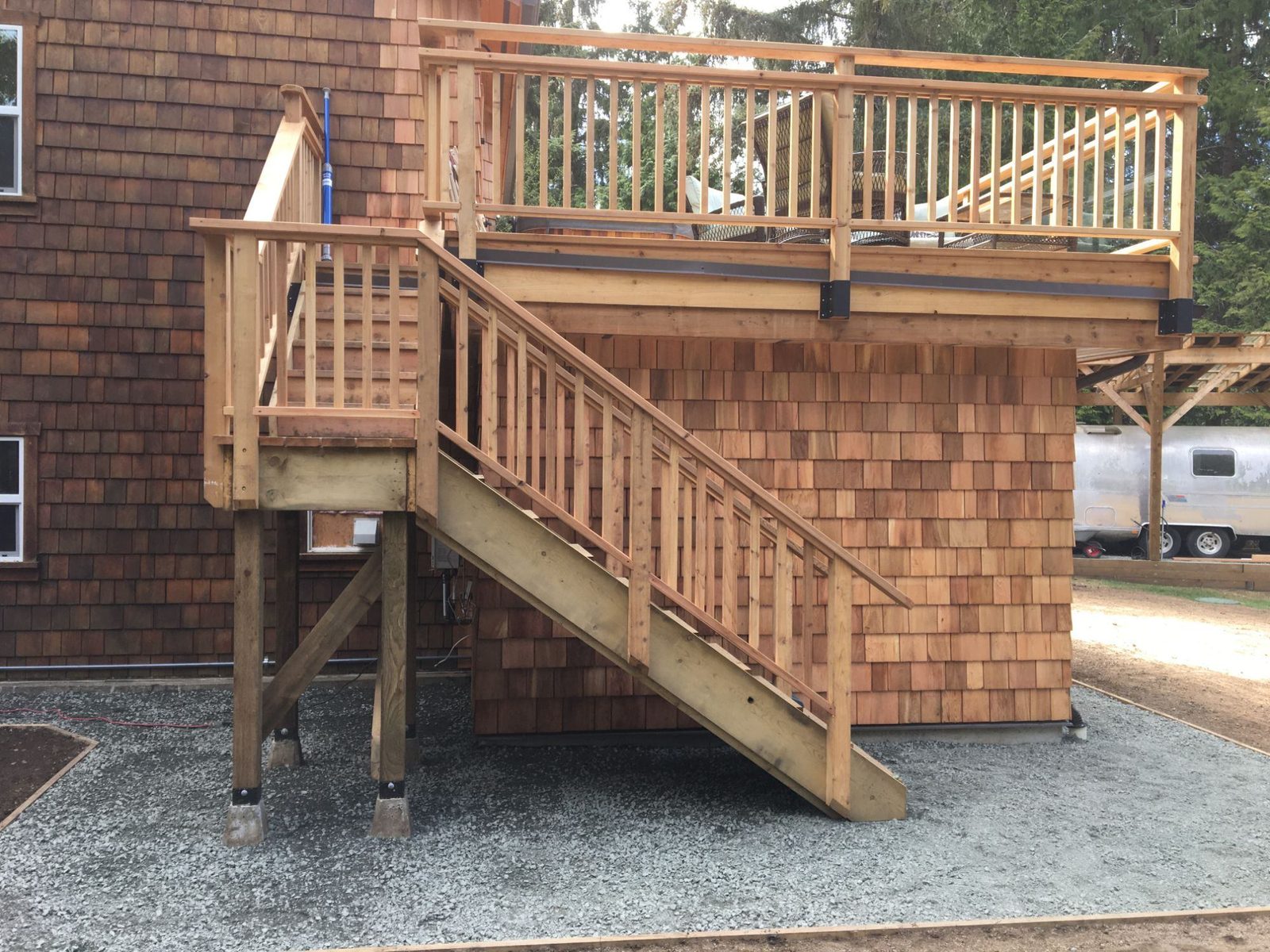 Elevated cedar-shingled hot tub deck with wood staircase and railing over gravel pad