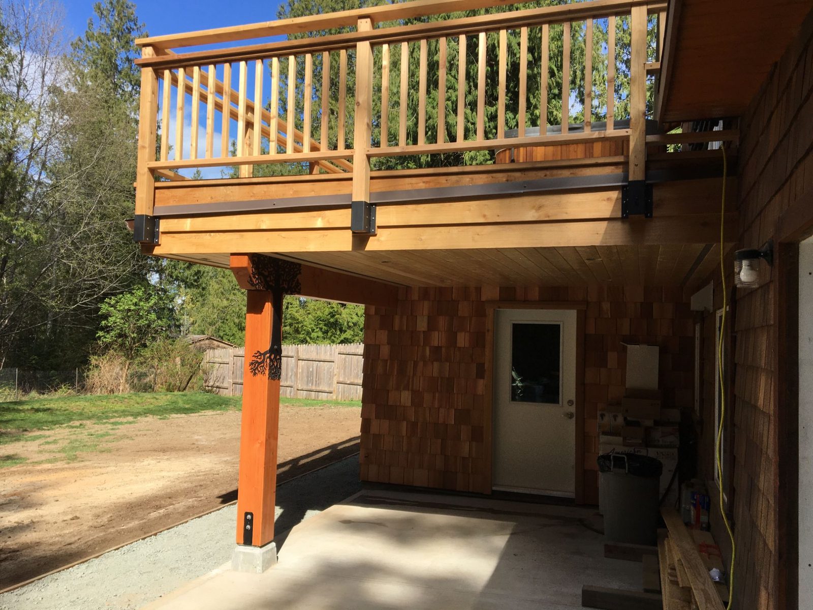 Underside of elevated cedar deck with timber post and railing over a patio in a forested yard