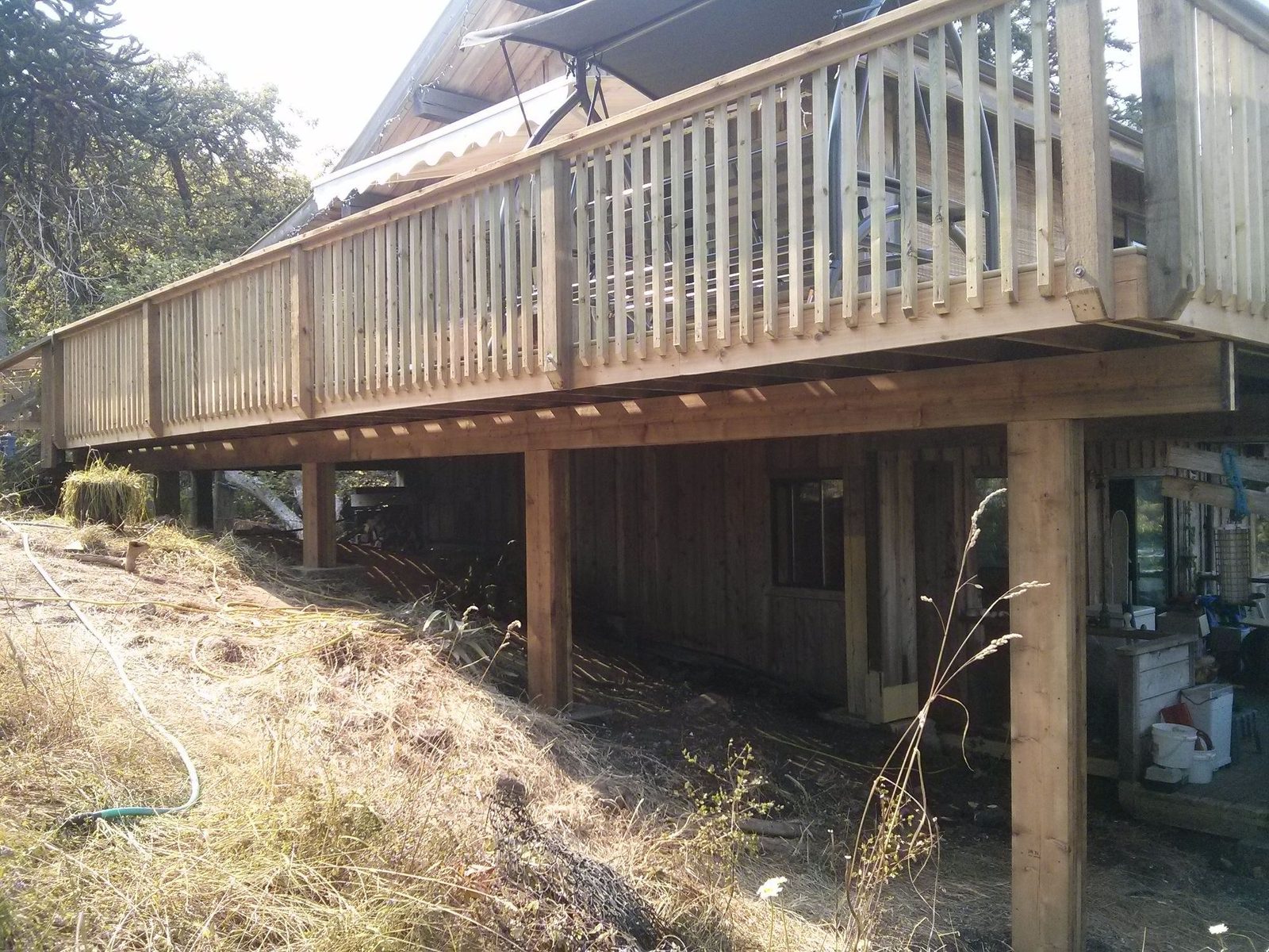 Long raised wood deck with railing on tall posts along a hillside home on a sunny day