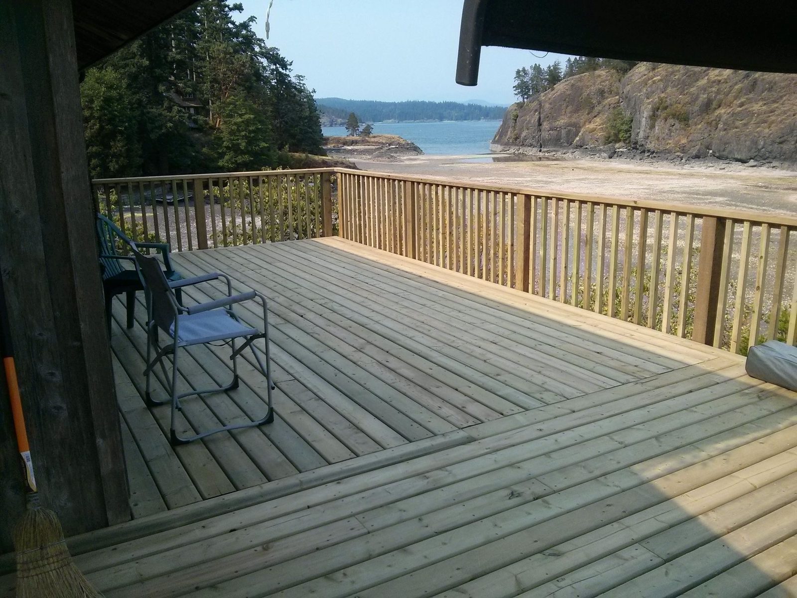 Wood deck with railing and chairs overlooking a tidal bay and rocky headland