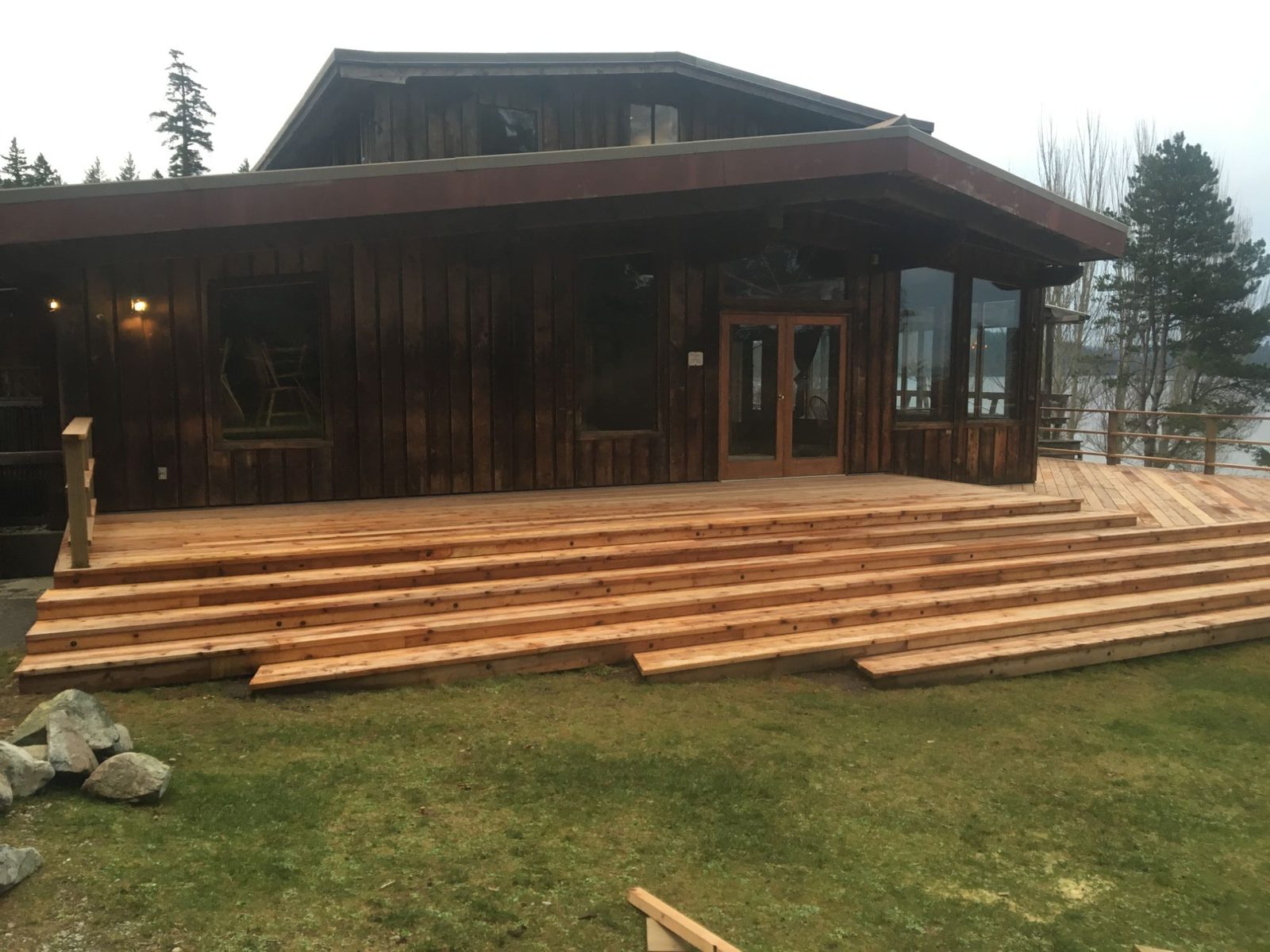 Wide low cedar deck with full-width tiered steps across the front of a dark wood waterfront home