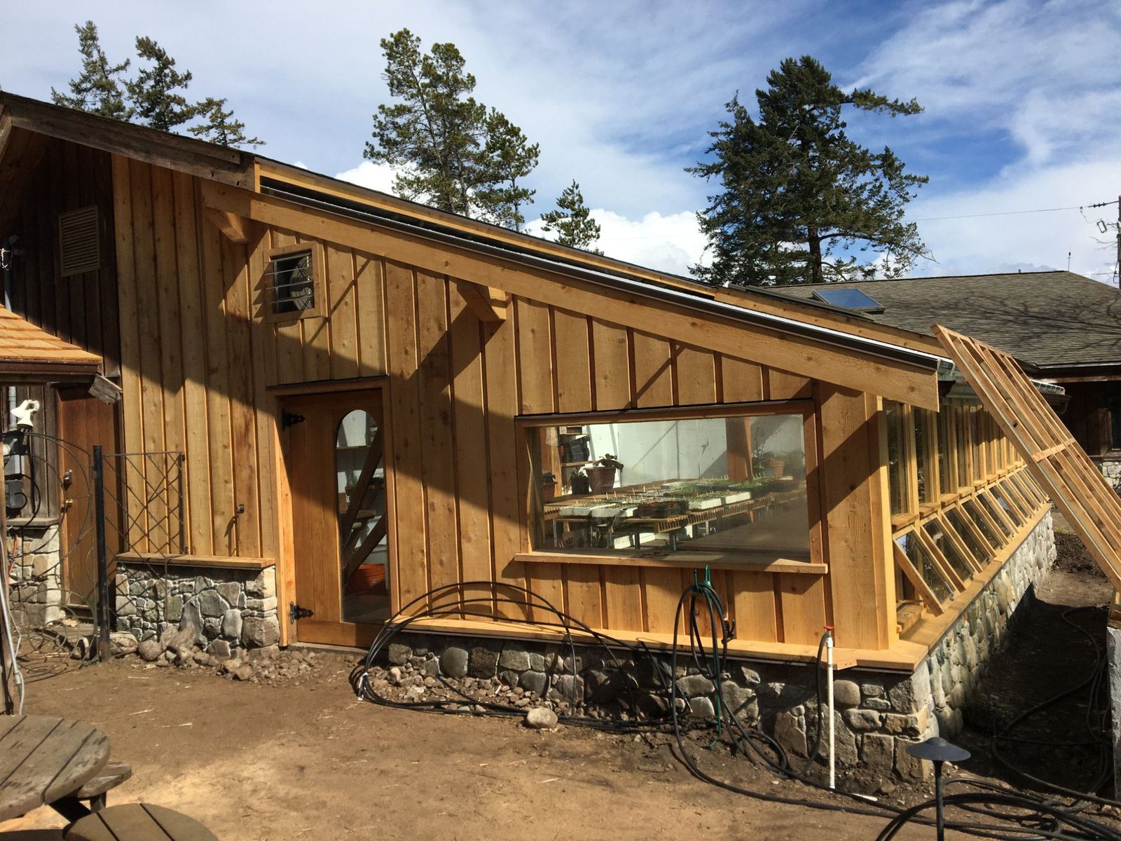 Greenhouse end wall with cedar board-and-batten siding, large window, wood door and stone foundation, Quadra Island