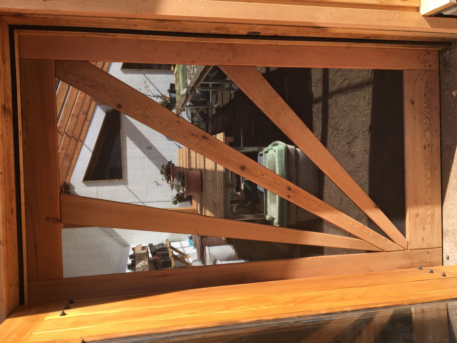 Close-up of fir timber-frame window with diagonal bracing and screen, reflecting the greenhouse and garden, Quadra Island