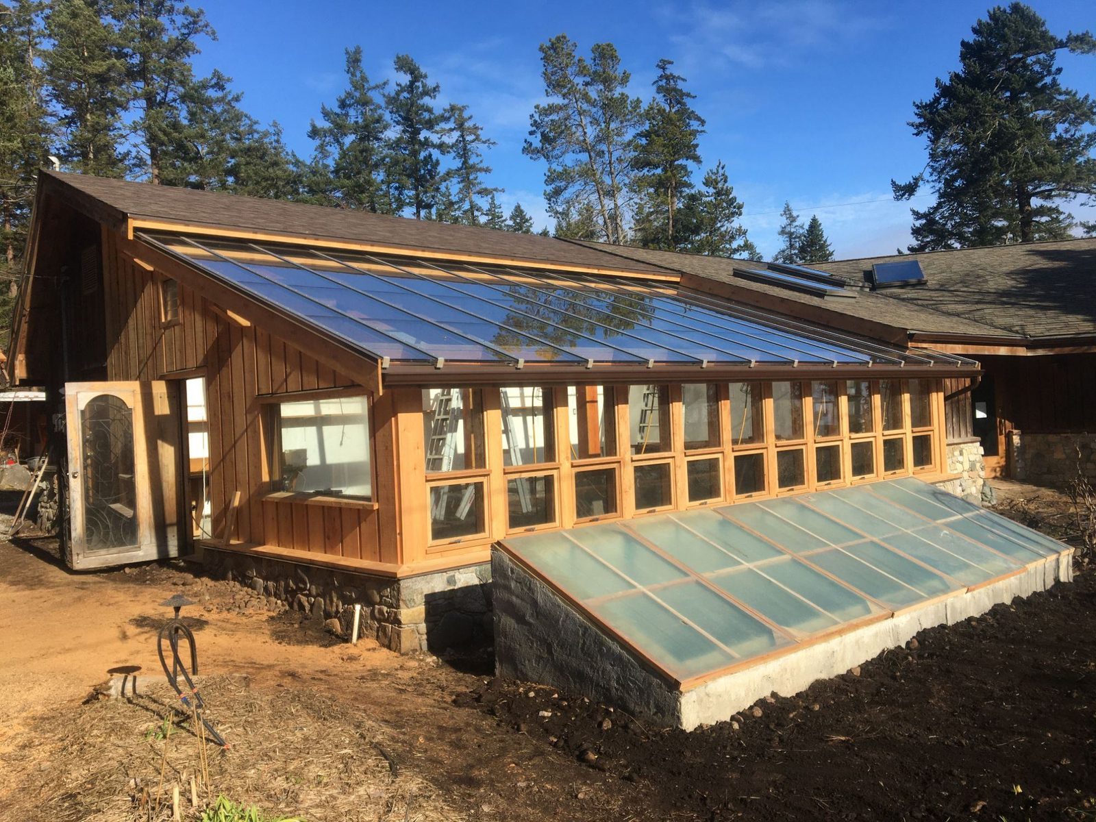 Timber-frame greenhouse with sloped glass roof and stone foundation on Quadra Island