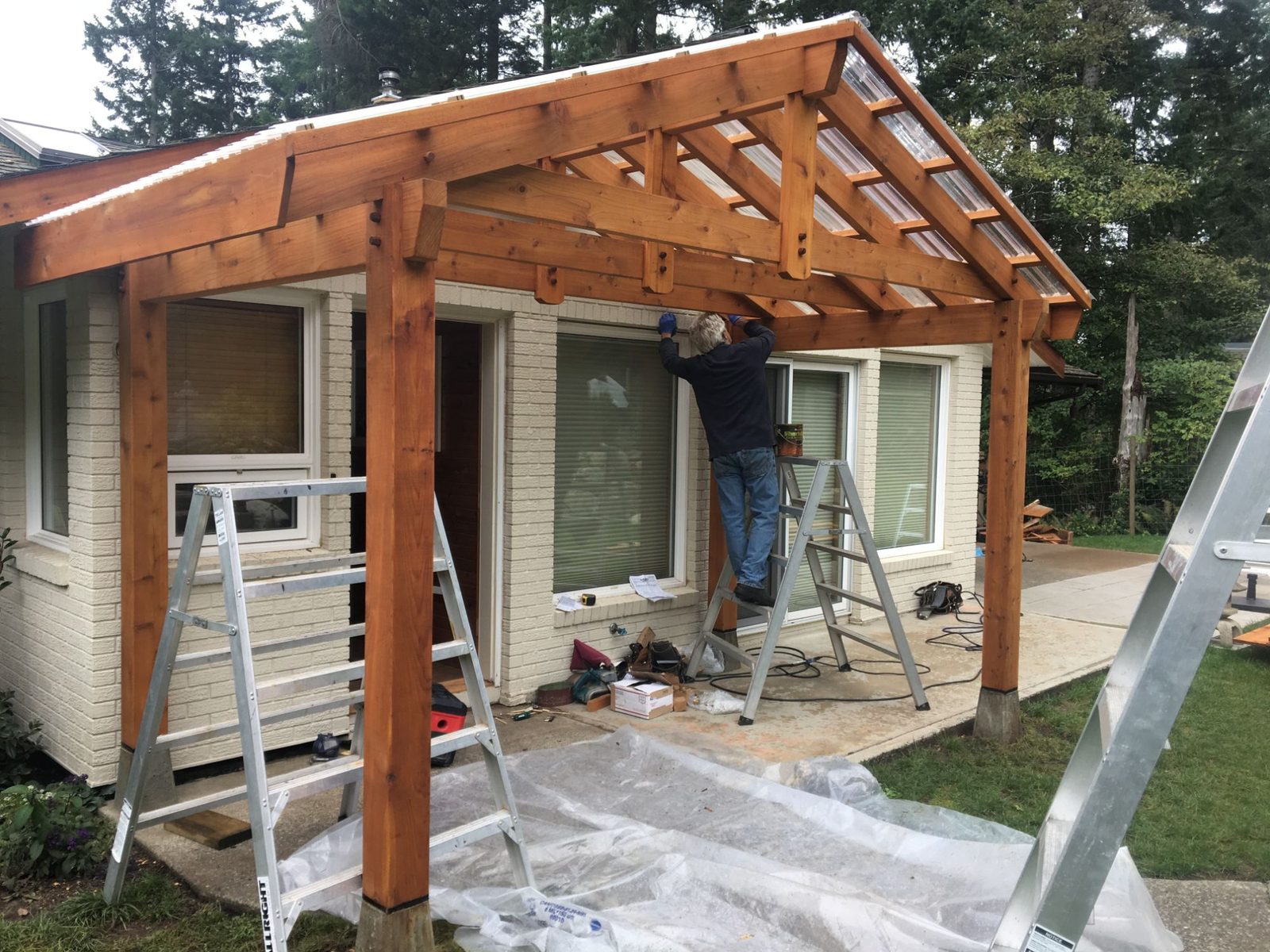 Timber frame porch with glass roof under construction on a house with a worker on a ladder