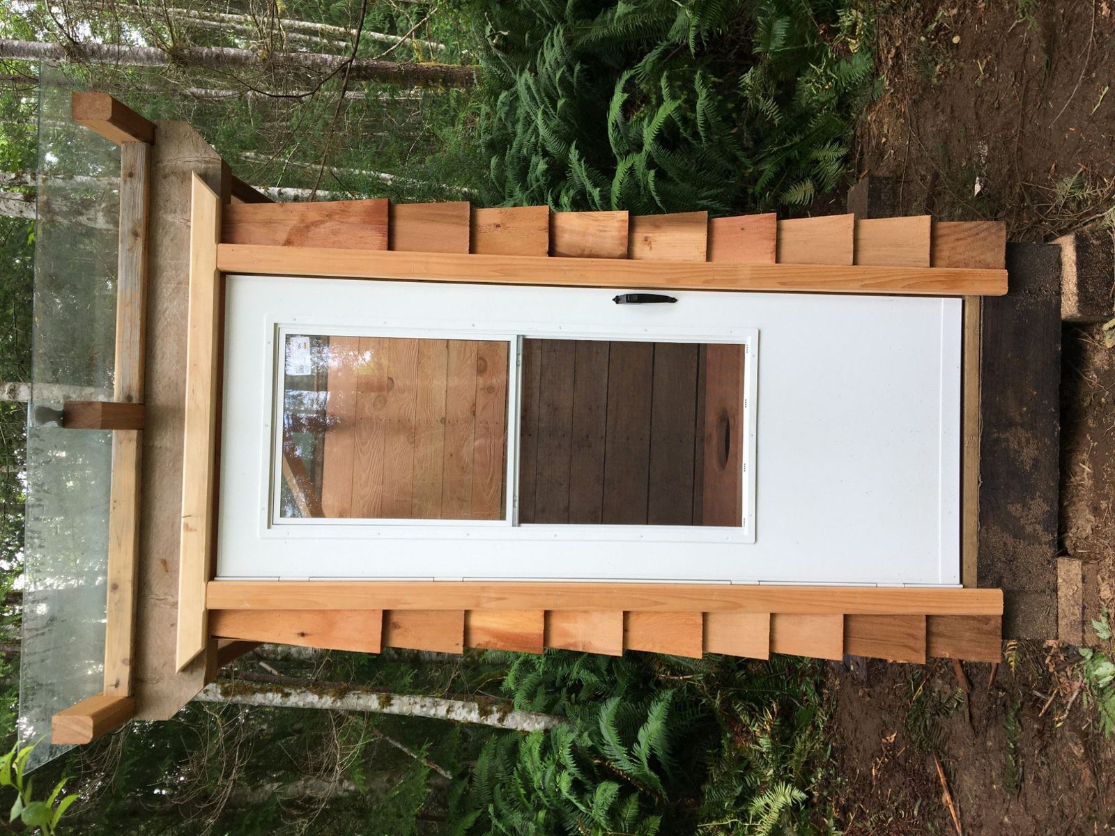 Custom built white door framed with rough cedar trim lying outdoors on forest ground on Quadra Island
