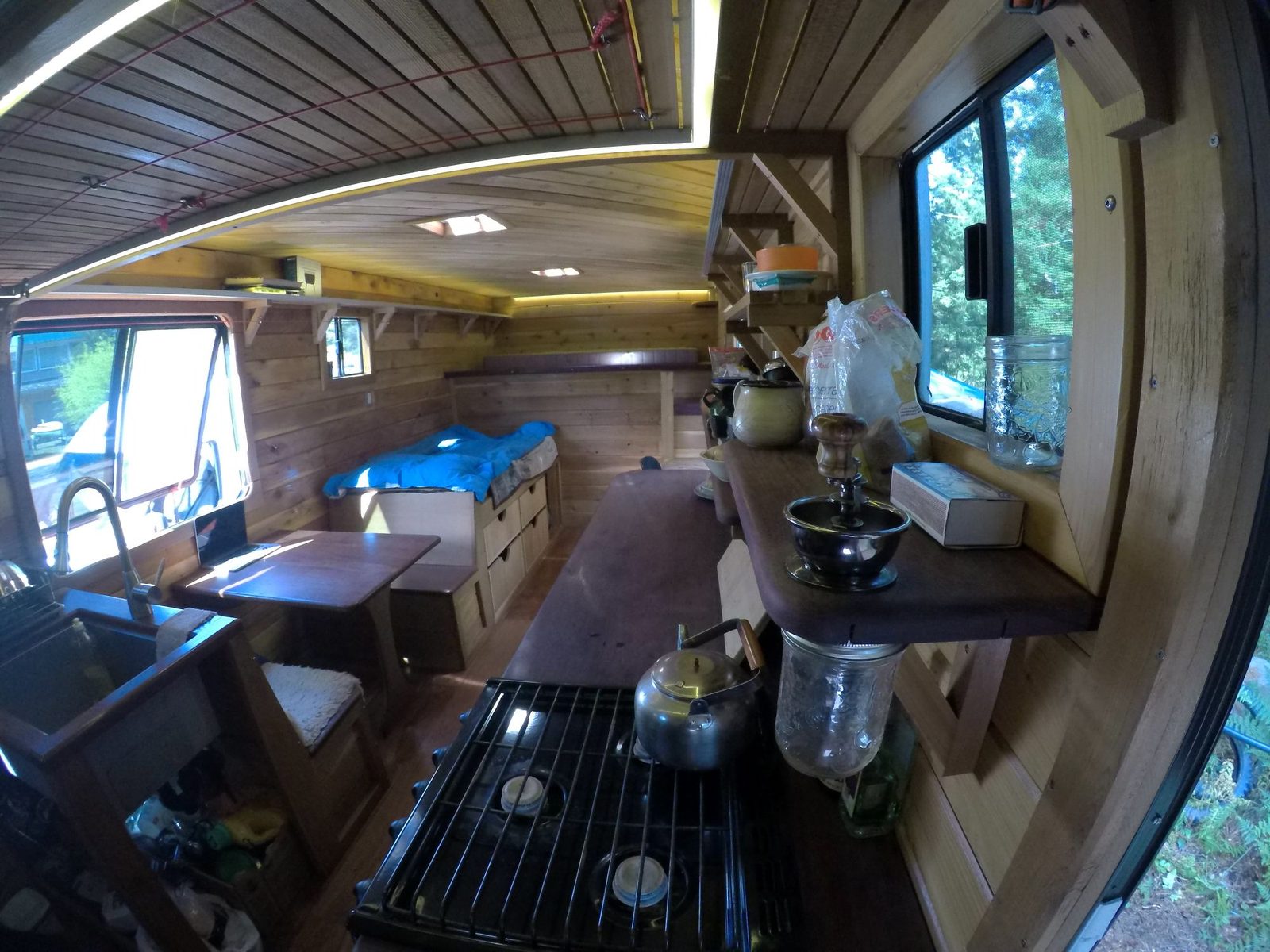 Tiny home interior with galley counter, propane cooktop, built-in bed and wood walls and ceiling on Quadra Island