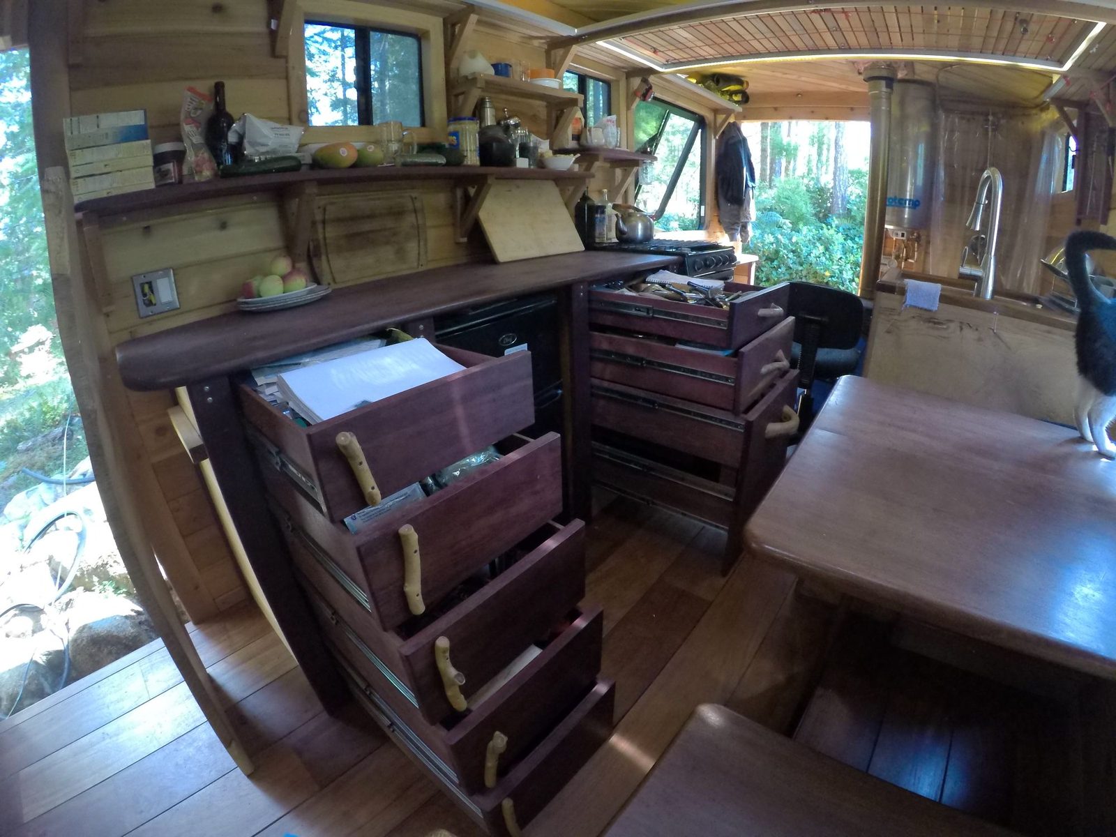 Custom wood dresser drawers and kitchen cabinetry open inside a curved-wall tiny home interior on Quadra Island
