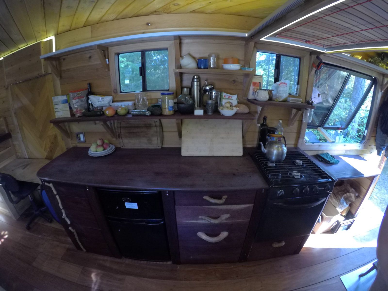 Tiny home wood kitchen with propane range, mini fridge and live edge counter surrounded by timber walls on Quadra Island
