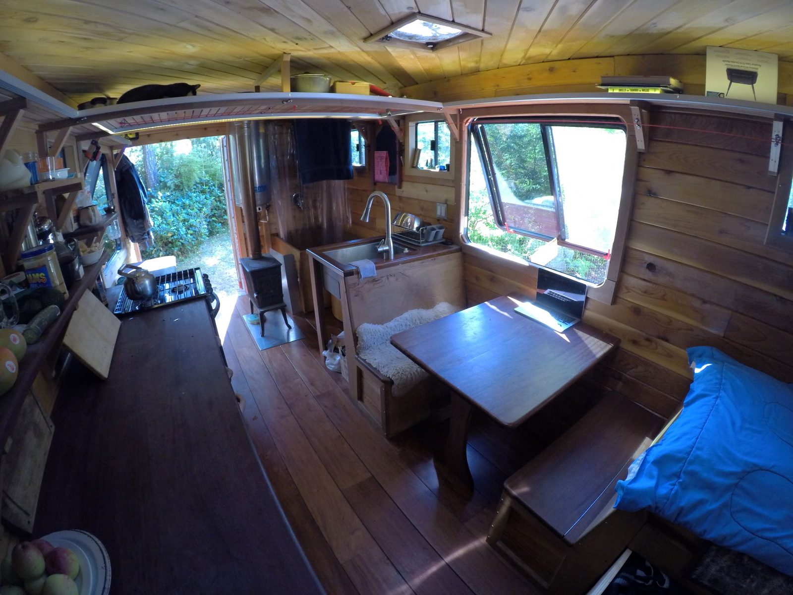 Tiny home interior with wood walls, dining nook, woodstove, kitchen sink and bench seating on Quadra Island
