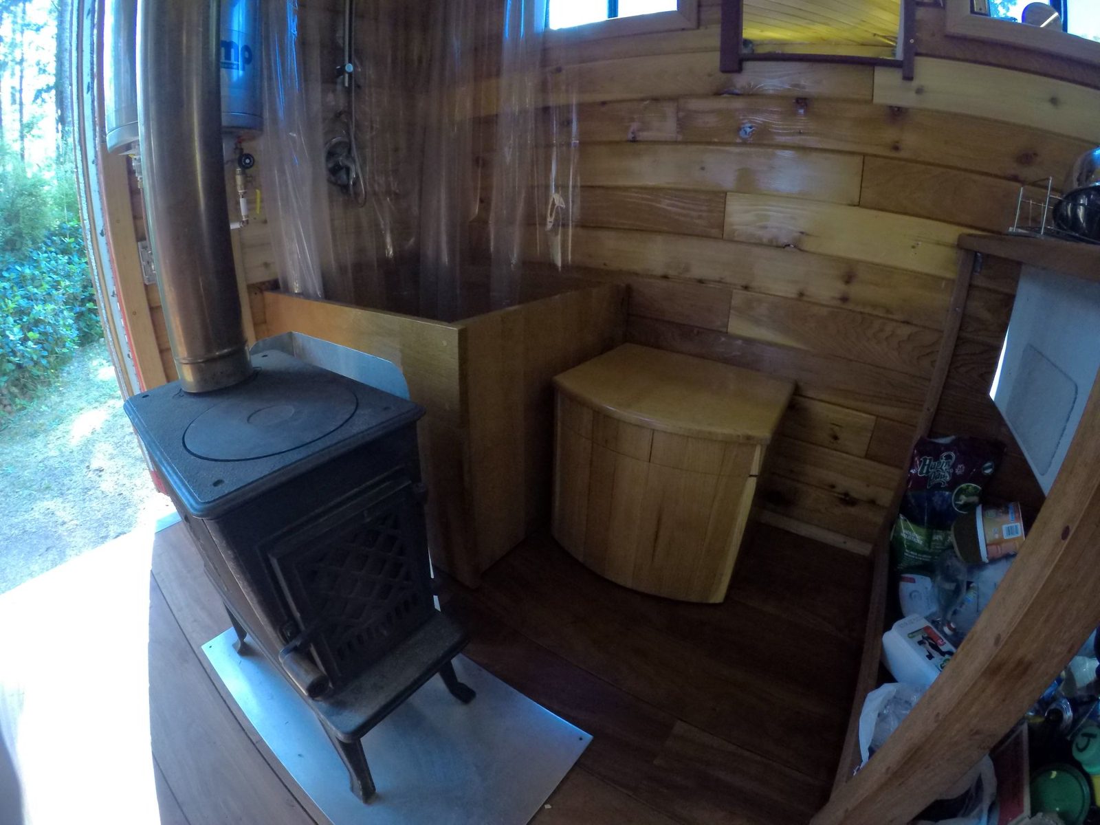 Cast iron woodstove and built-in wood bench in a curved cedar-walled tiny home interior on Quadra Island