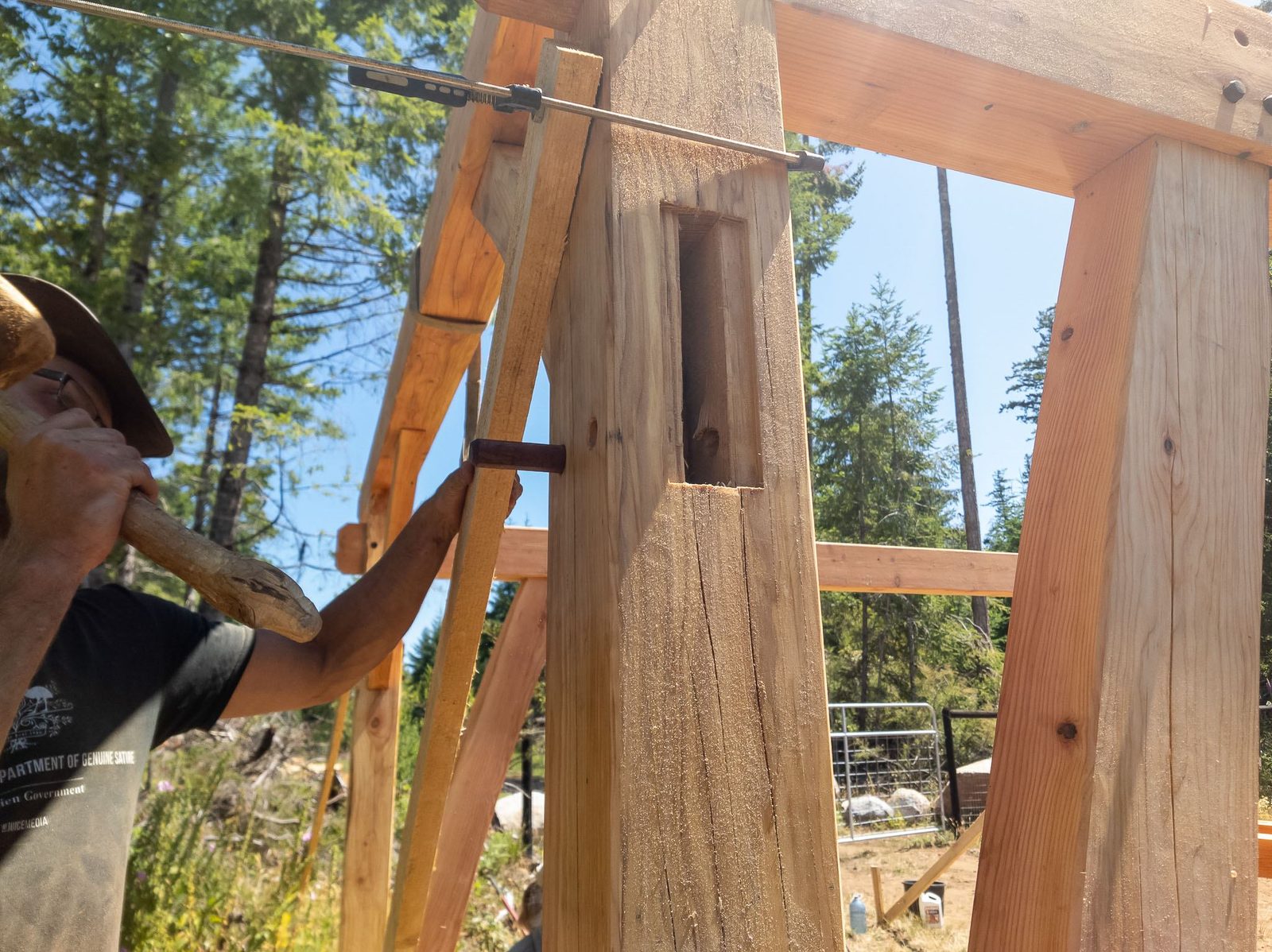 Close view of a carpenter pegging a mortise-and-tenon joint on a timber frame post on Quadra Island