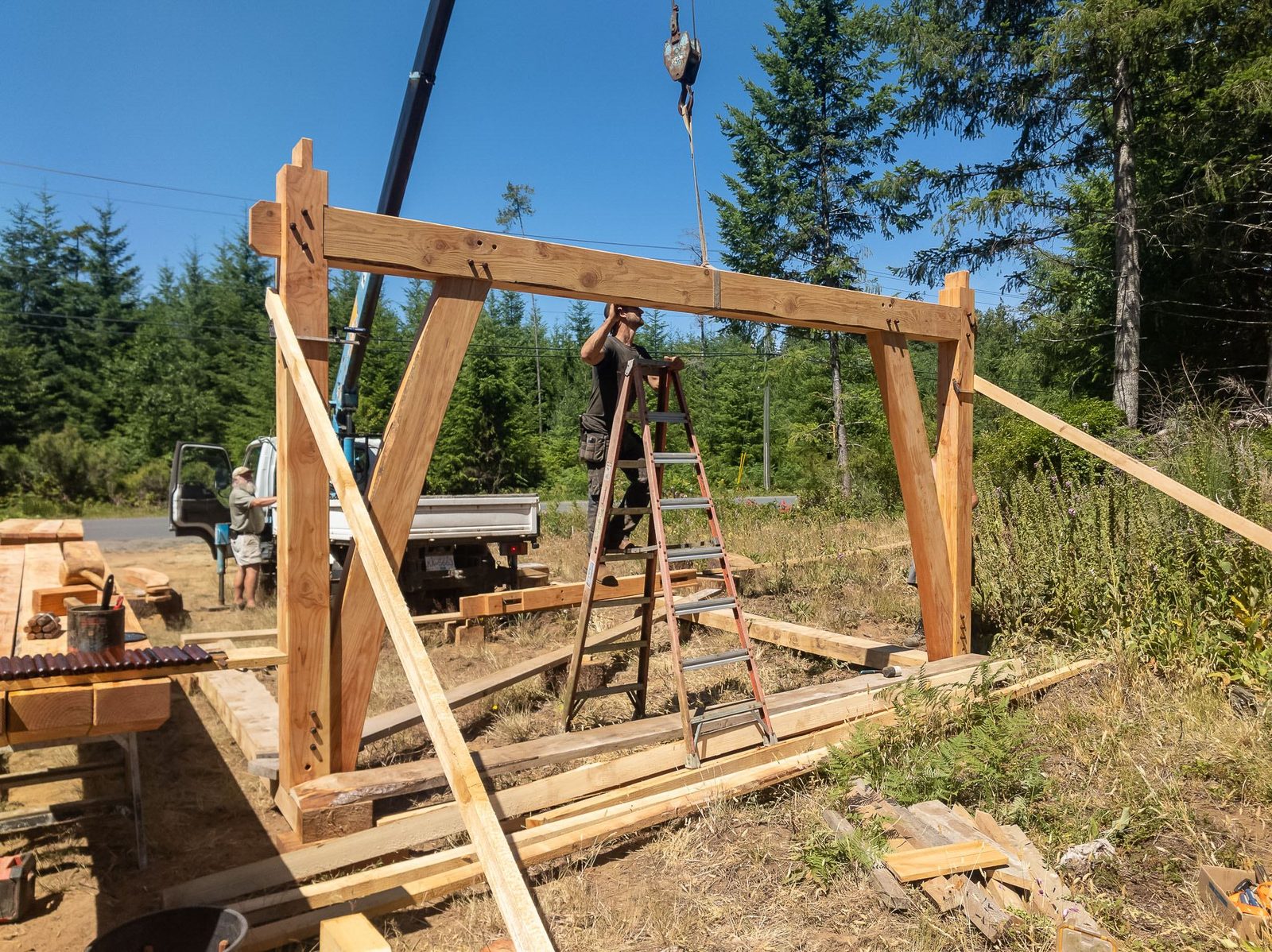 Assembled timber frame bent with knee braces standing under a crane on Quadra Island