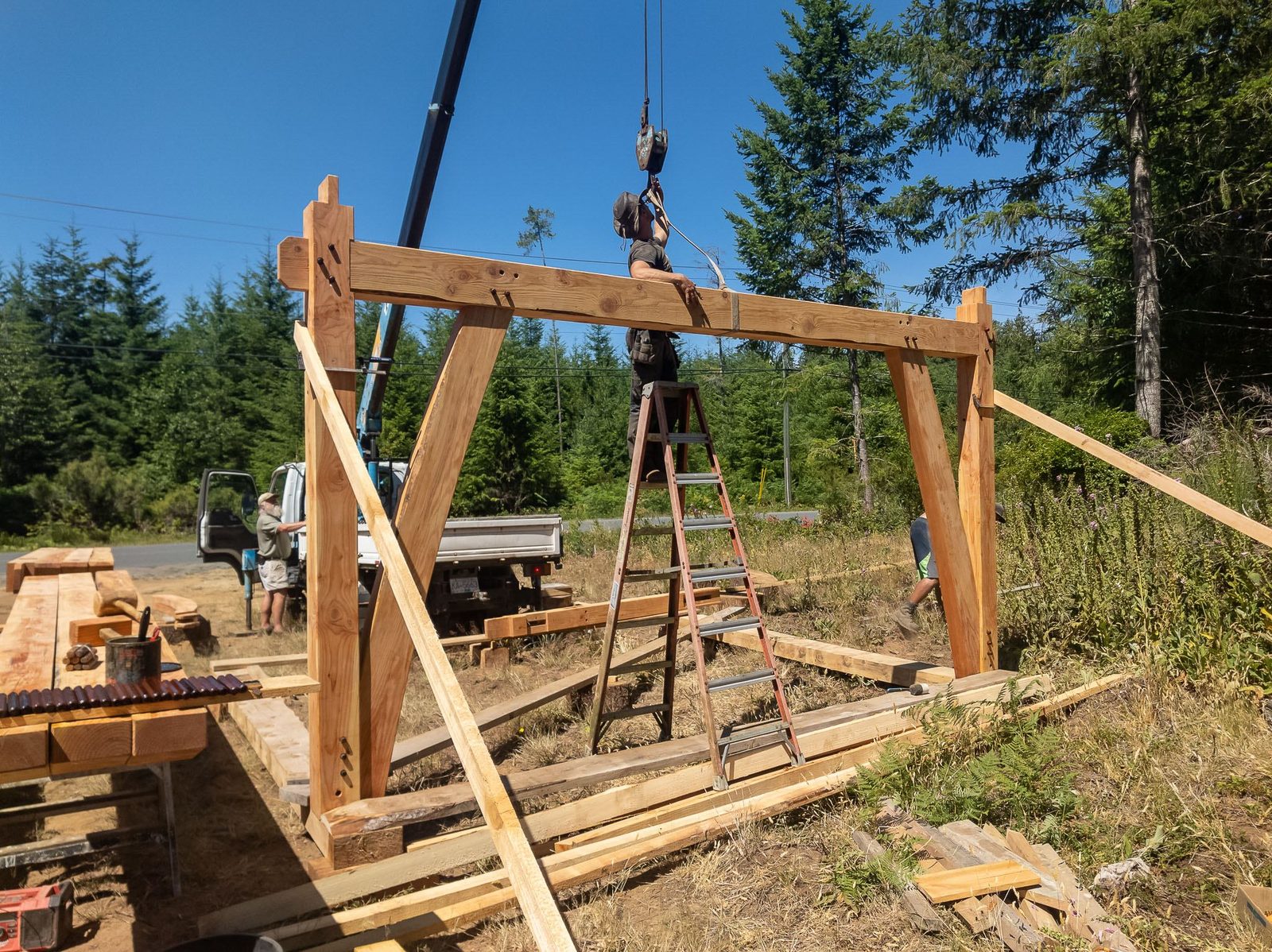 Timber frame bent with posts, tie beam and knee braces braced upright under a crane on Quadra Island