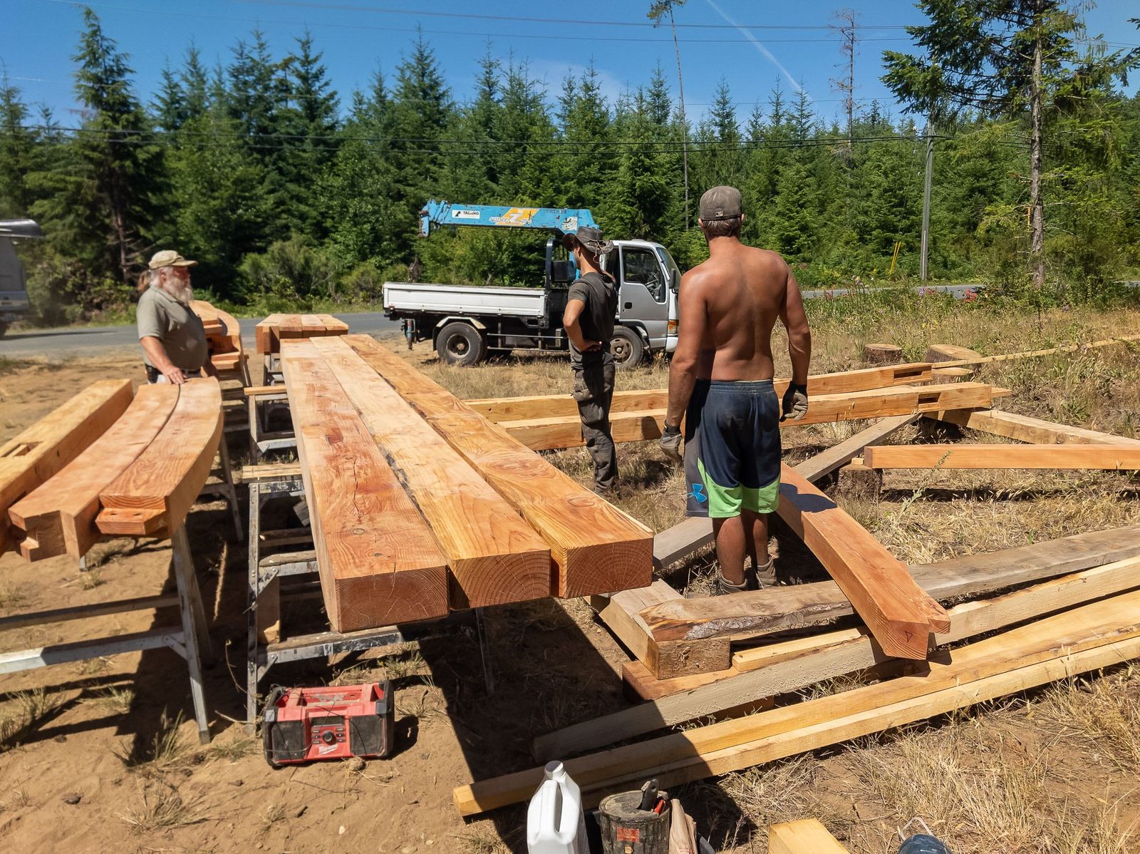 Carpenters arranging long timber frame beams on sawhorses with a crane truck behind on Quadra Island