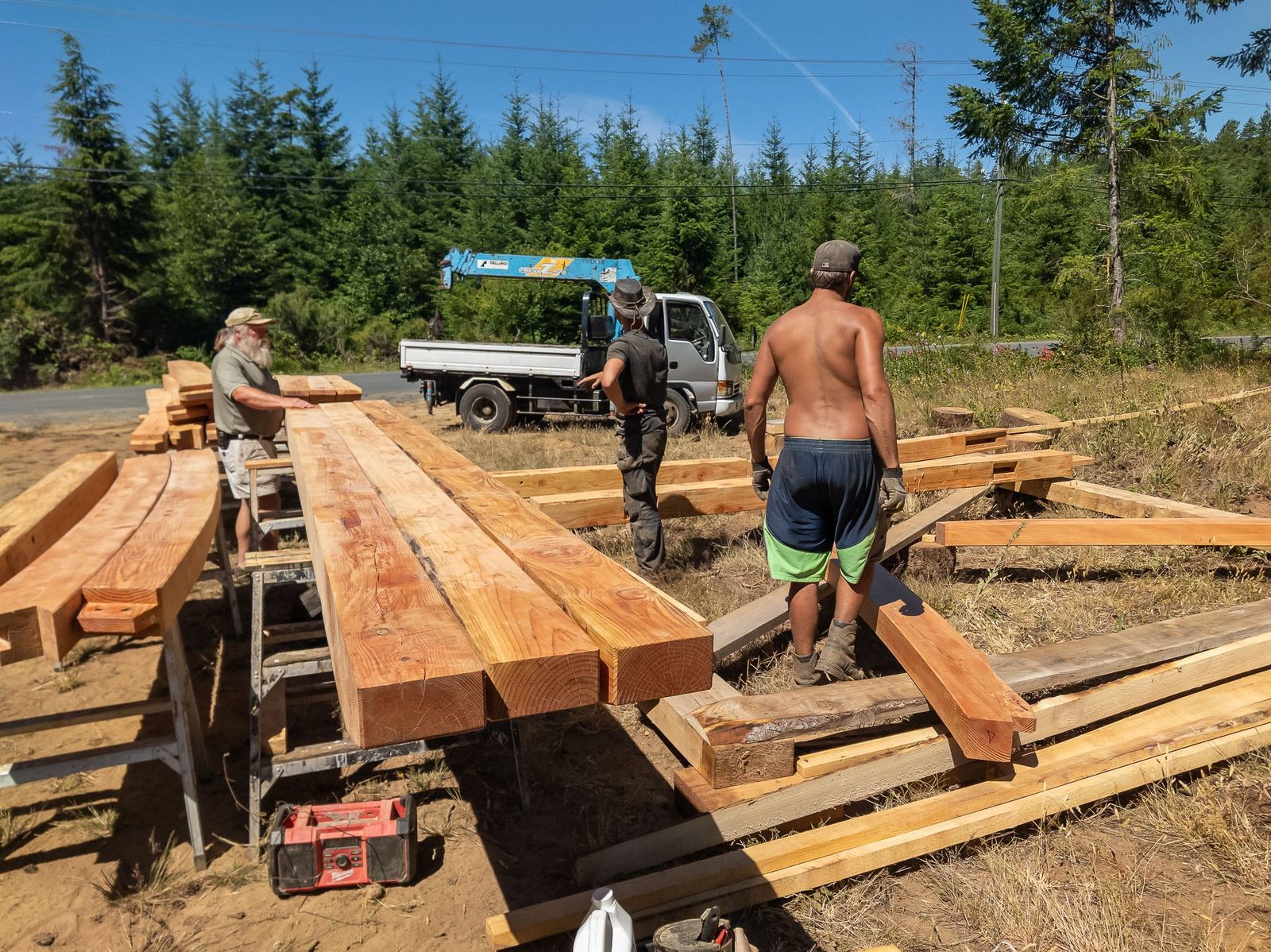 Workers handling milled timber frame beams beside a flatbed crane truck on Quadra Island