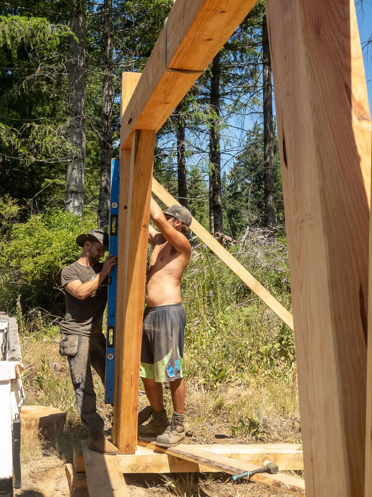 Two carpenters checking a timber frame post for plumb with a long blue level on Quadra Island