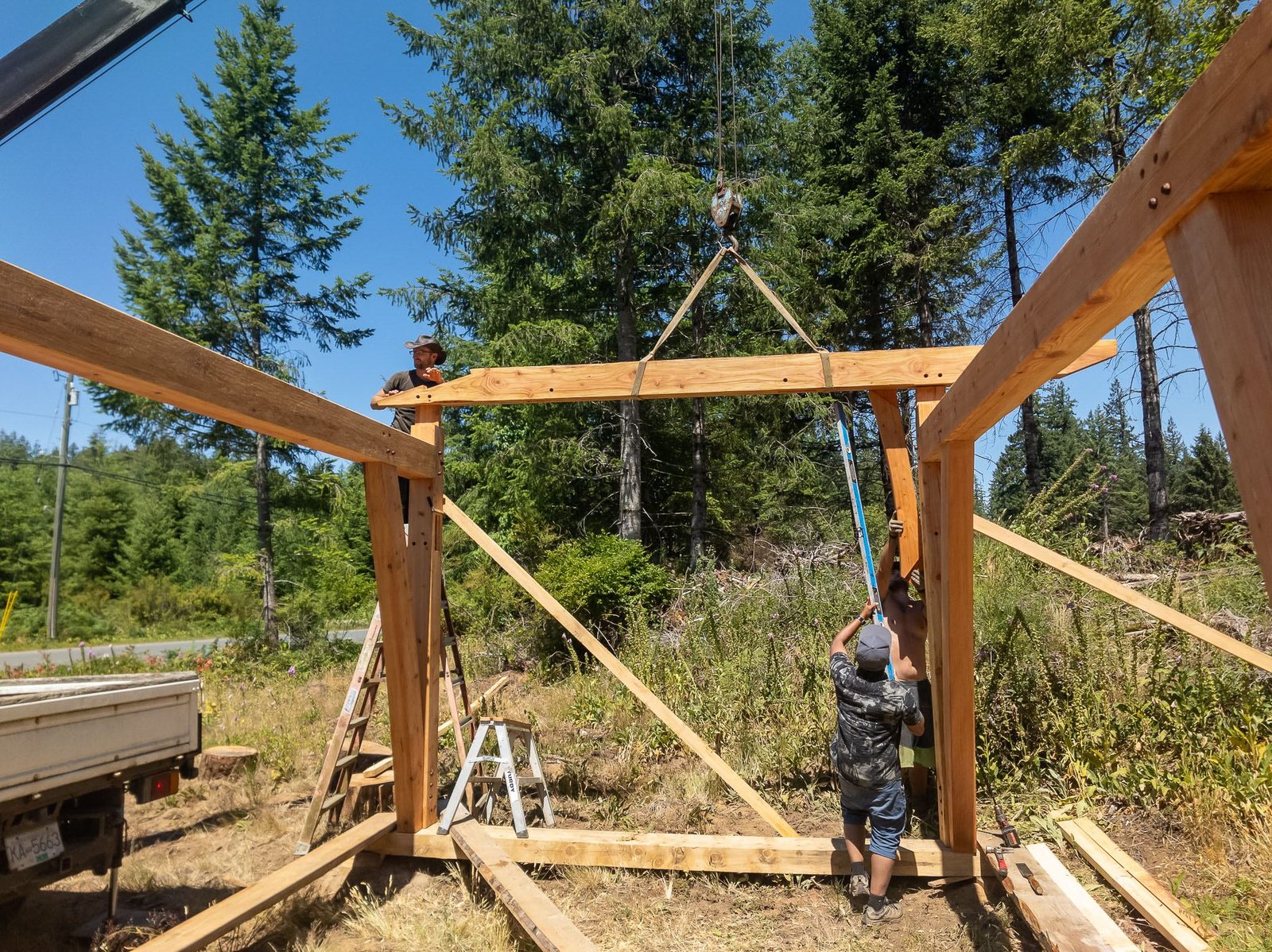 Crane-lifted connecting beam set between two timber frame bents with carpenters guiding it on Quadra Island