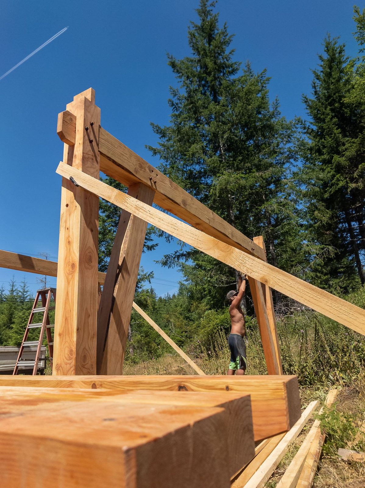 Carpenter guiding a knee brace into a timber frame bent seen from a low angle on Quadra Island
