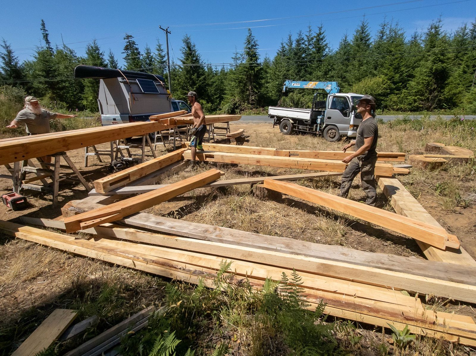 Workers laying out timber frame floor members in a clearing with truck and camper on Quadra Island