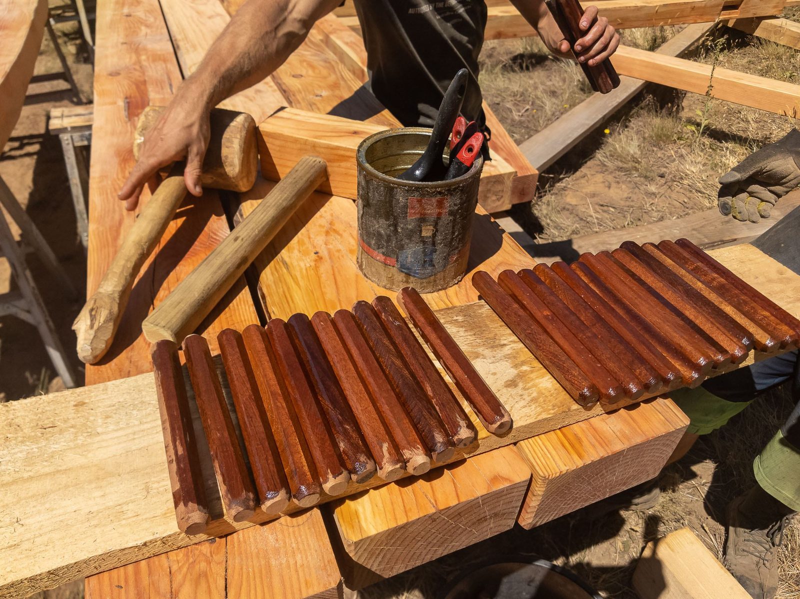 Carpenter reaching past stained wooden trunnels and a wooden mallet on a timber frame work bench on Quadra Island