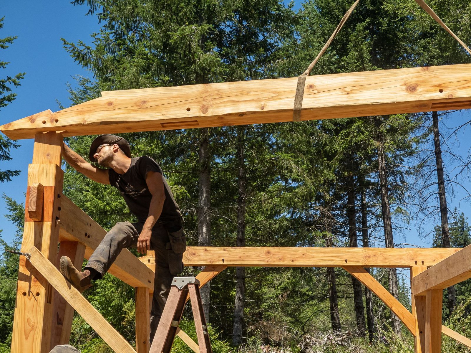 Carpenter positioning a crane-lifted rafter overhead on a timber frame bent on Quadra Island