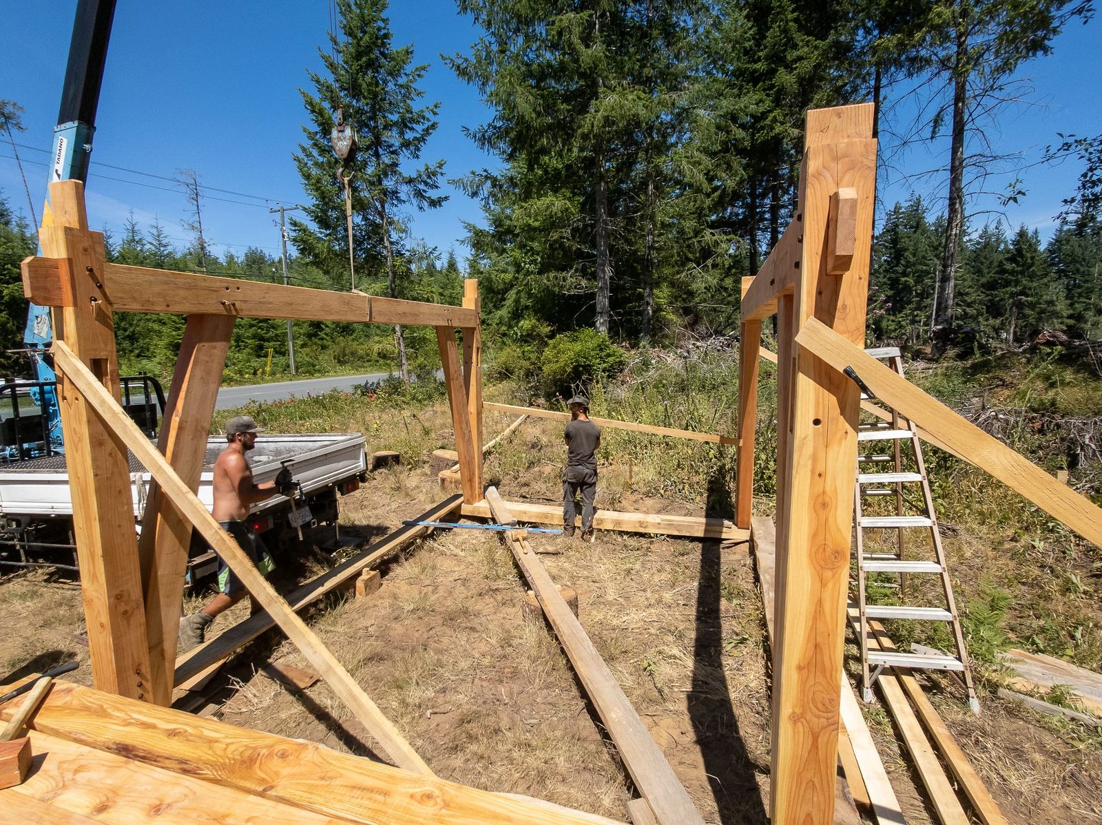 Two timber frame bents standing upright with a crane and worker between them on Quadra Island