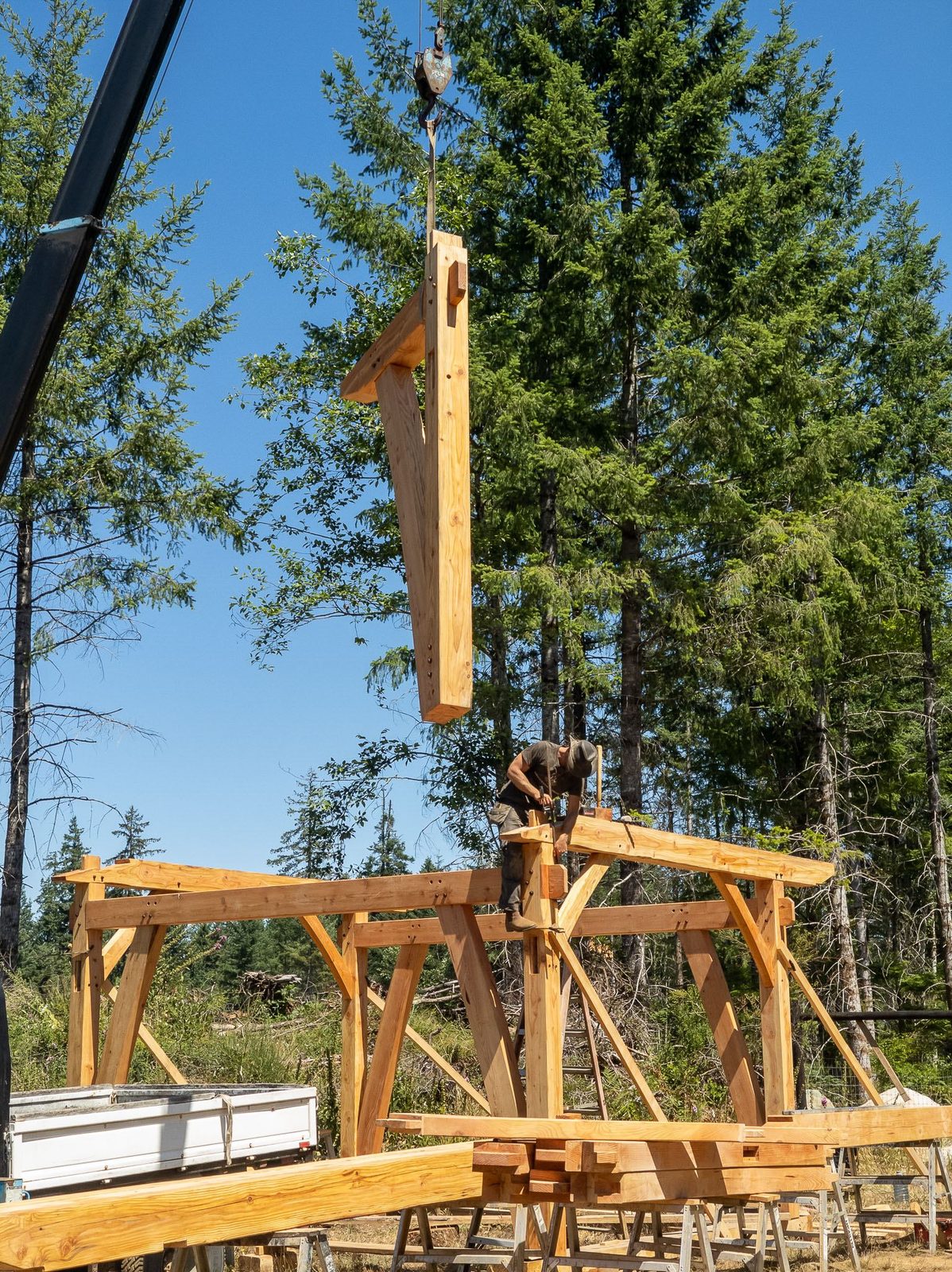 Crane lowering a timber rafter toward a carpenter atop the raised timber frame on Quadra Island