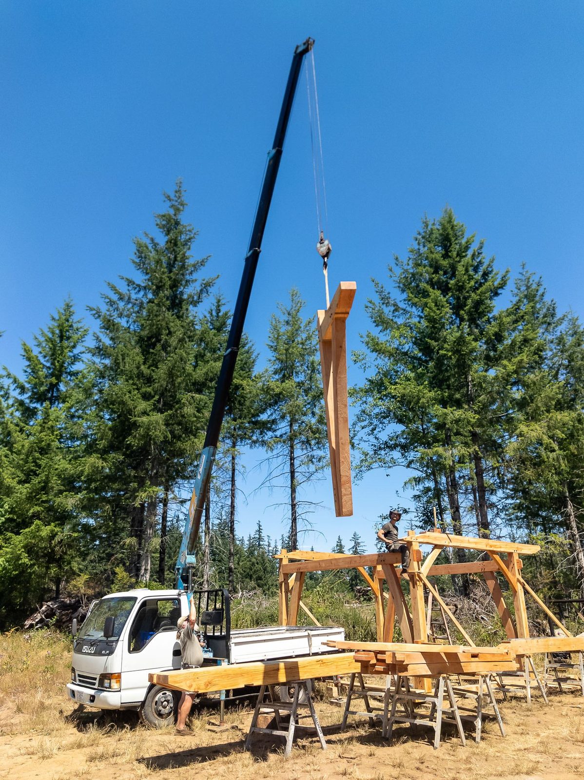 Timber rafter member suspended from a crane boom over the frame and crane truck on Quadra Island
