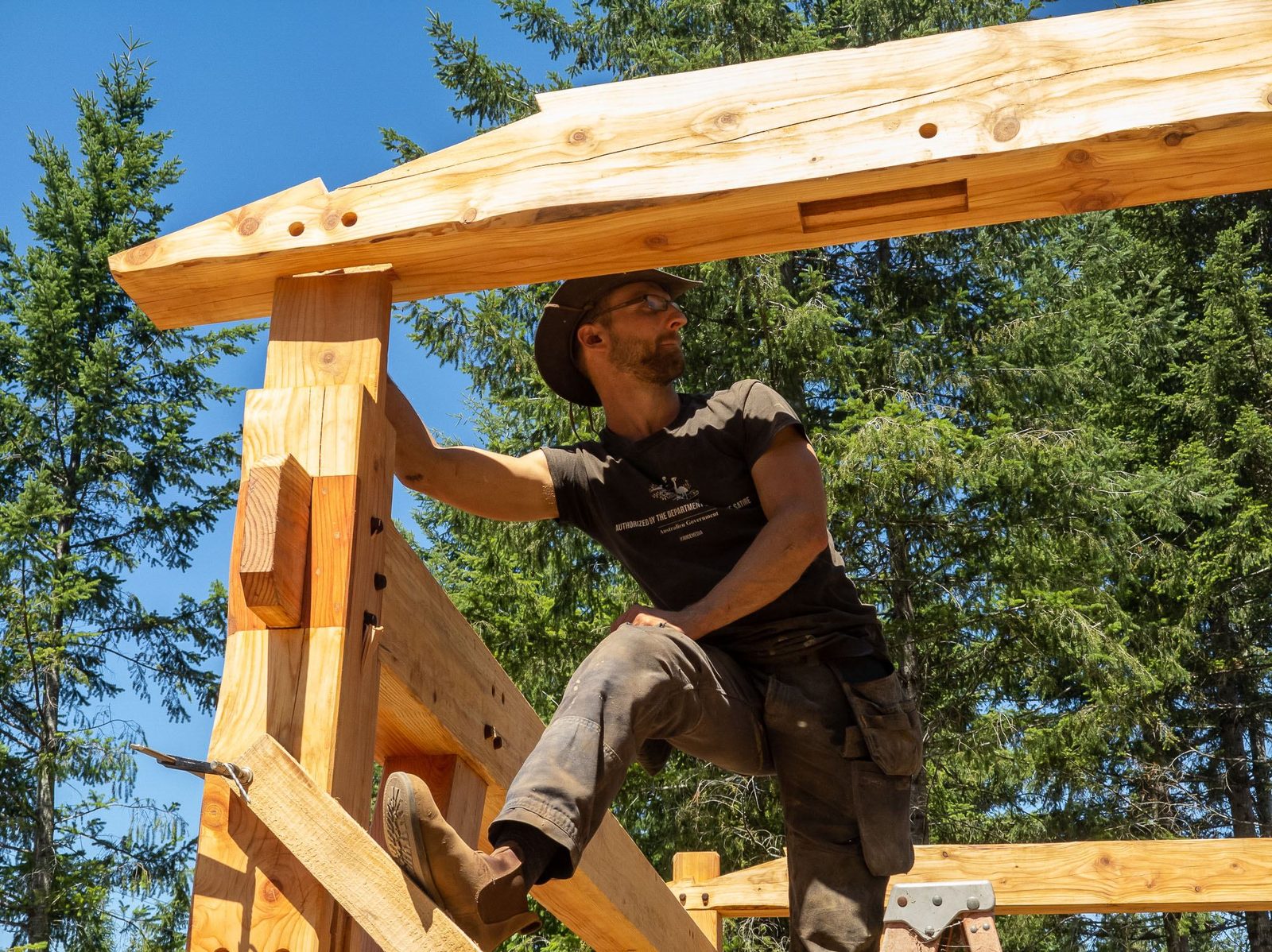 Carpenter fitting a rafter to a timber frame post-top tenon viewed from a low angle on Quadra Island