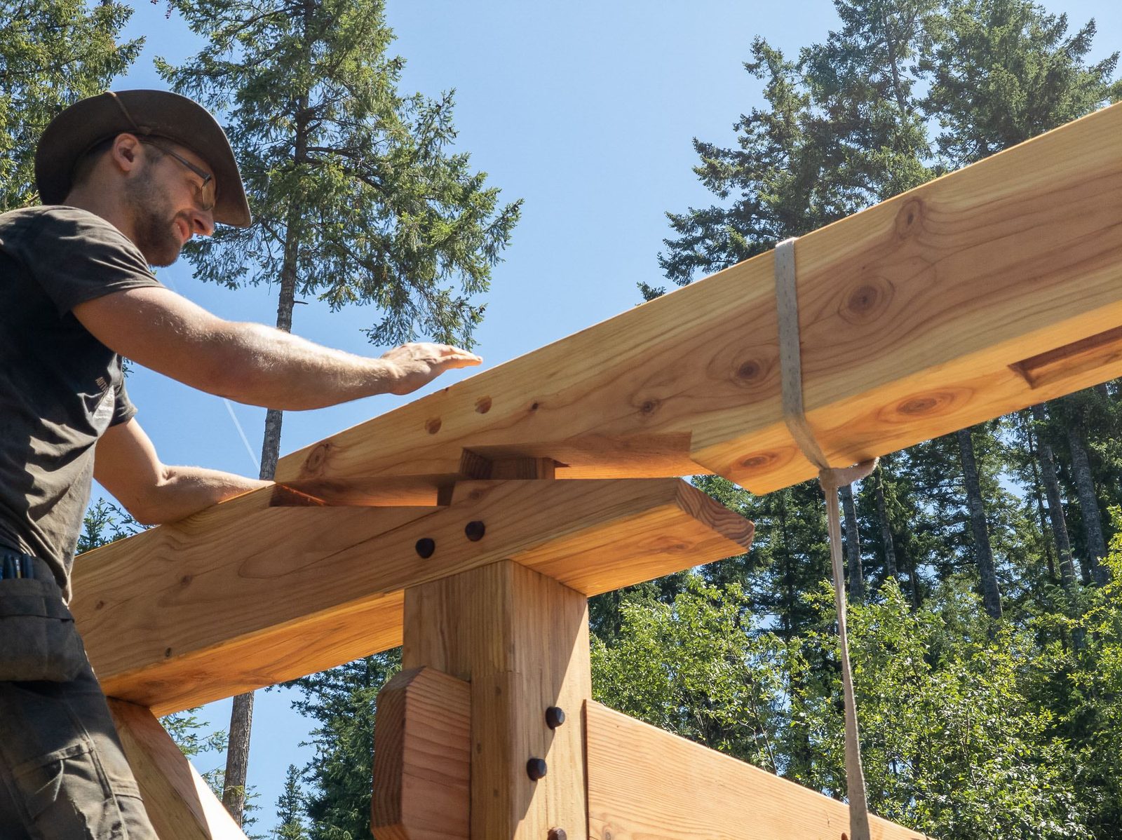 Close low-angle view of a carpenter seating a rafter onto pegged timber frame plate joinery on Quadra Island