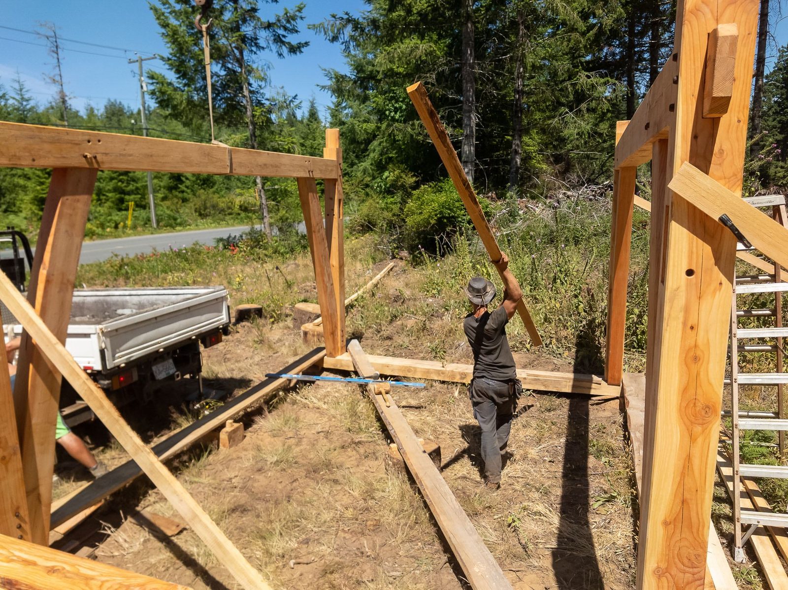 Carpenter lifting a timber frame post upright by hand within the partly framed floor on Quadra Island