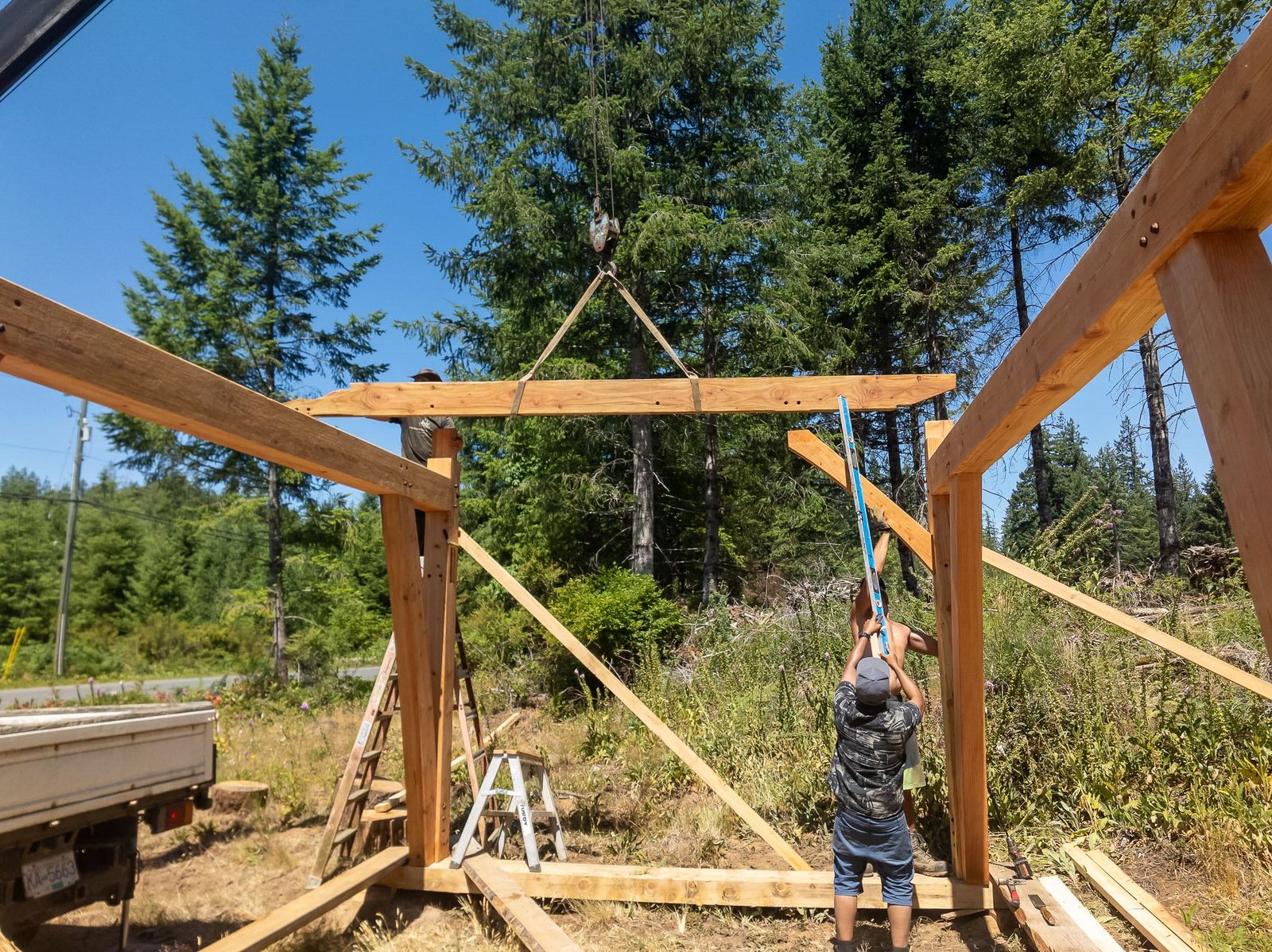 Carpenter rigging a crane-suspended beam between two timber frame bents on Quadra Island