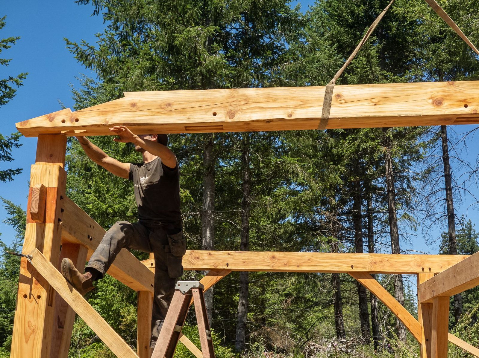 Carpenter on a ladder guiding a long rafter onto the top plate of a timber frame on Quadra Island