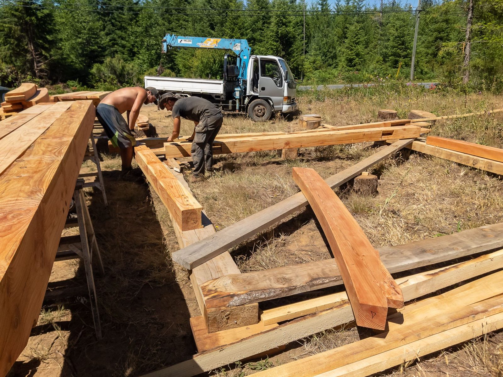Carpenters fitting timber frame sill beams on the ground with a crane truck behind on Quadra Island