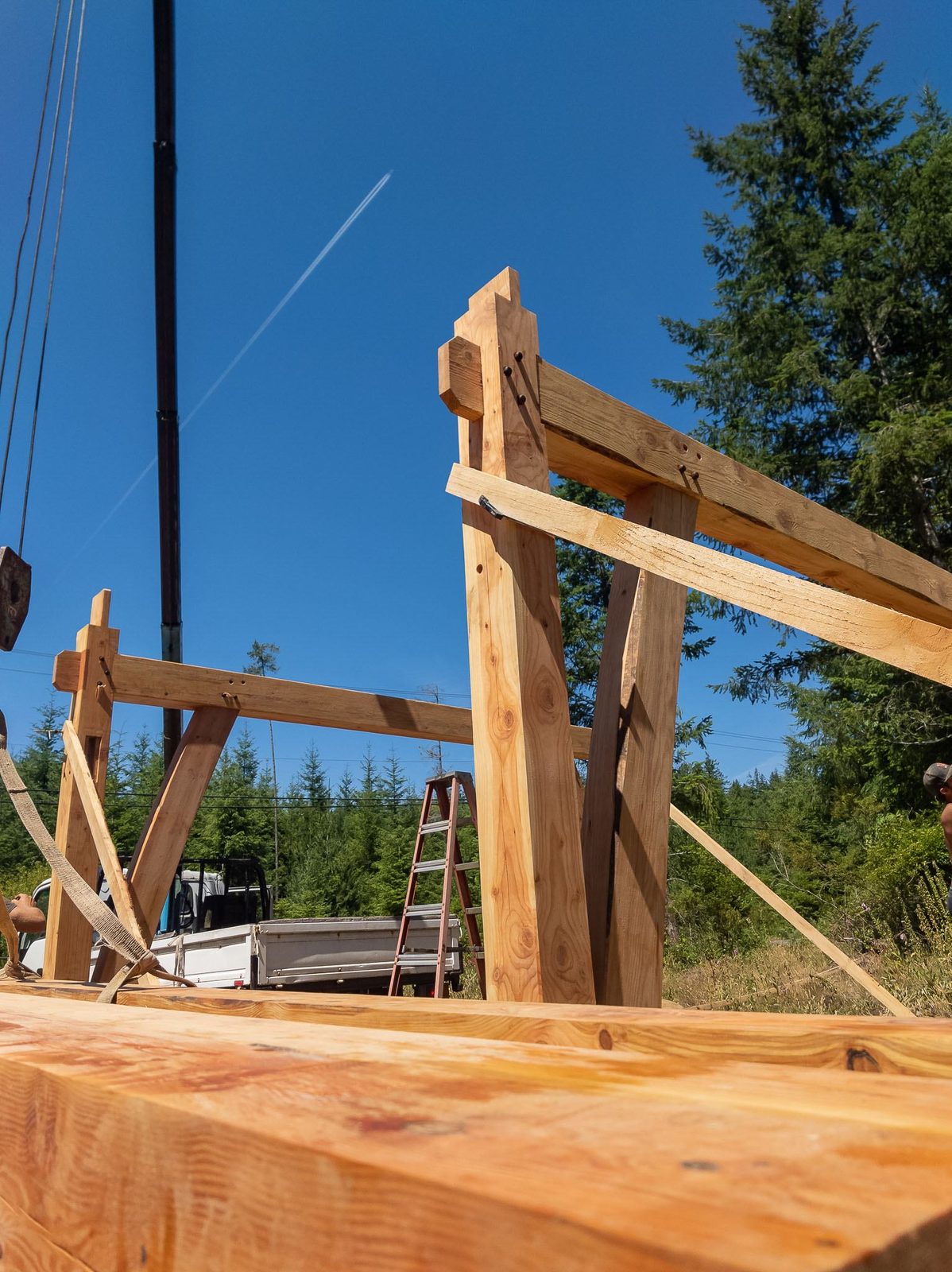 Low-angle view of timber frame posts and braces meeting a tie beam against clear blue sky on Quadra Island