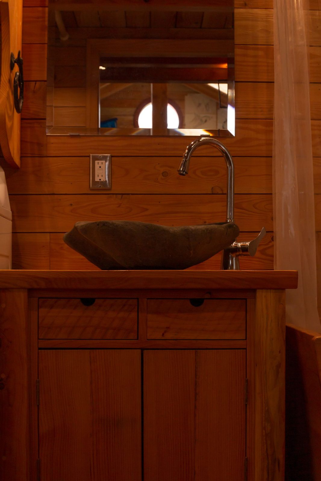 Stone vessel sink on a wood vanity with mirror and gooseneck faucet in a tiny home bathroom