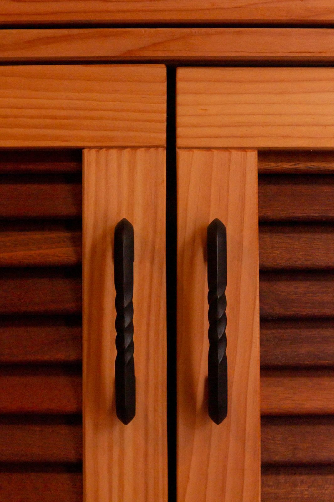 Hand-forged black iron pulls on louvered wood cabinet doors in a tiny home