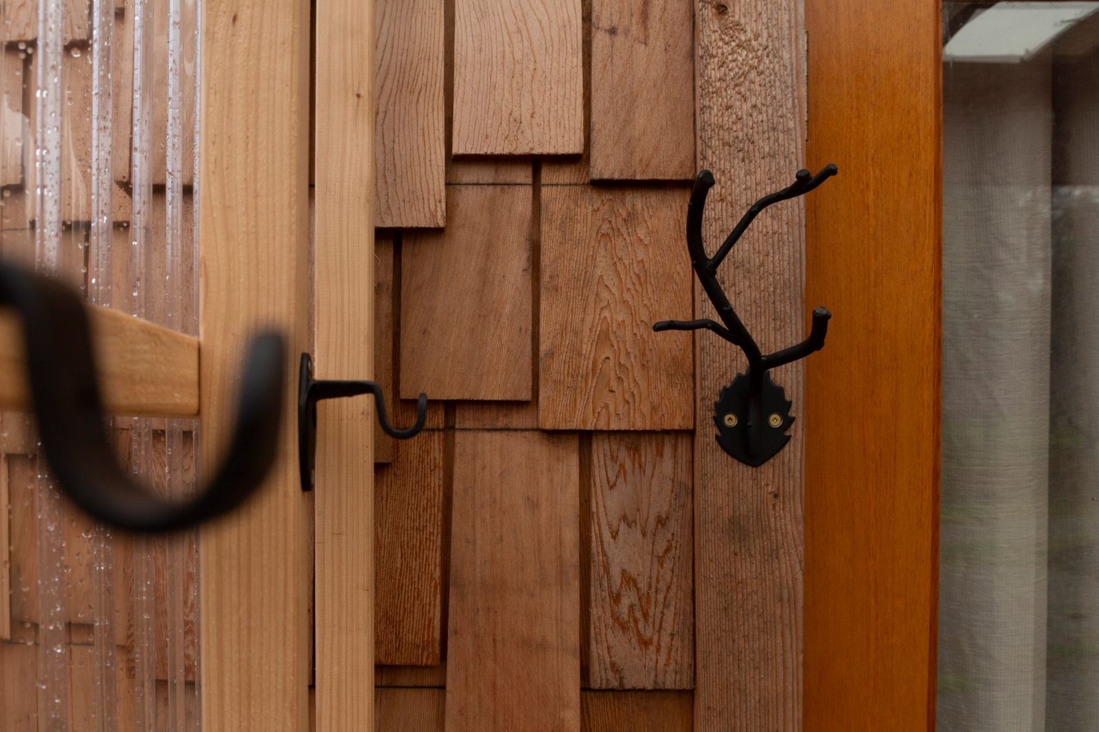 Iron coat hooks mounted on cedar shingle and trim siding of a tiny home porch on Quadra Island