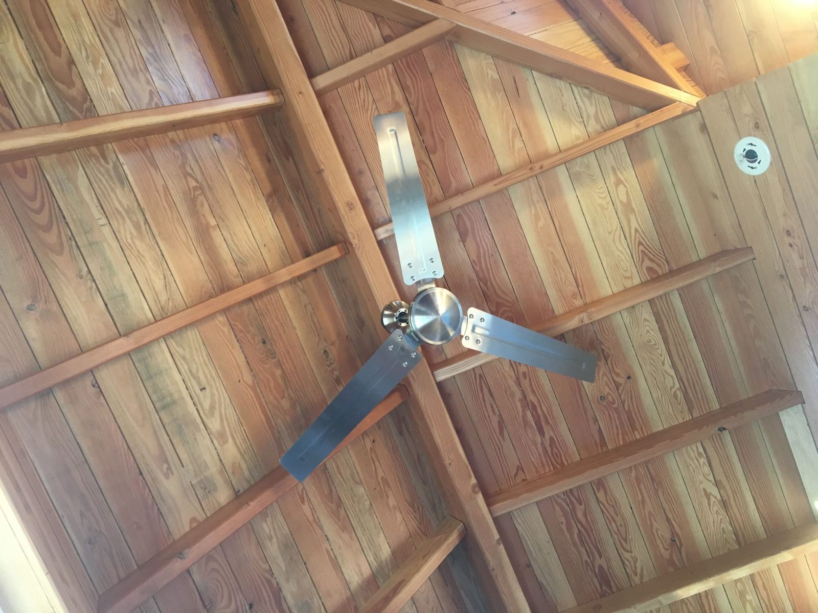 Wood-paneled vaulted ceiling with exposed beams and a metal ceiling fan inside a tiny home