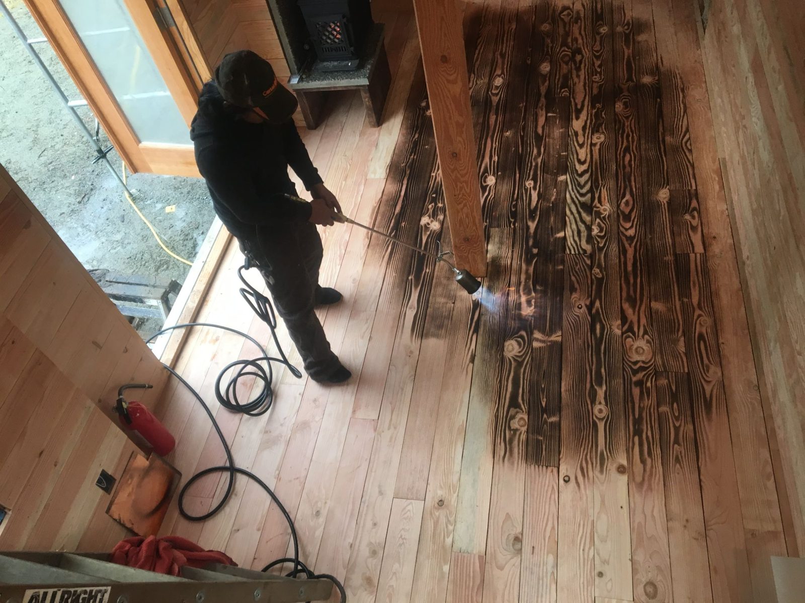 Worker torch-finishing reclaimed wood plank flooring inside a tiny home interior