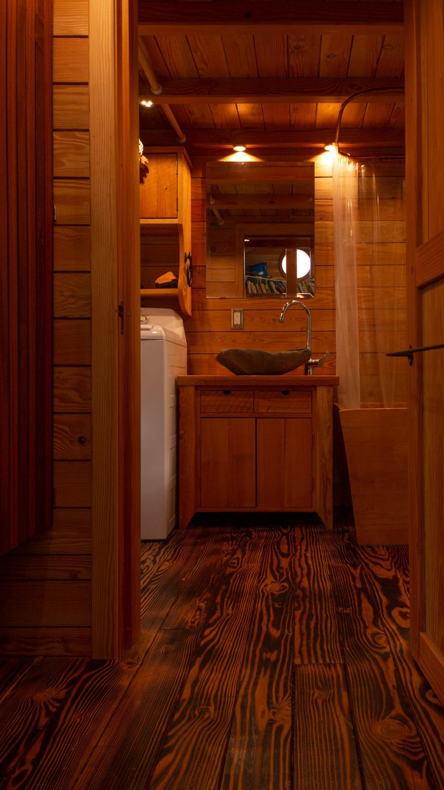 Tiny home bathroom with stone vessel sink, wood vanity and mirror over reclaimed wood floor