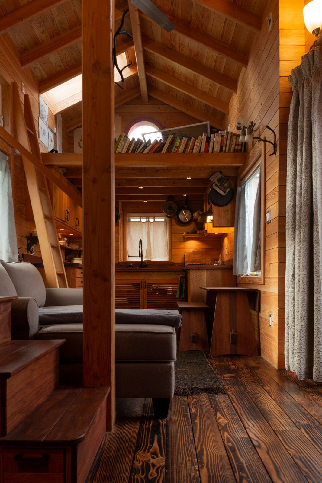 Tiny home interior with sofa, loft ladder, bookshelf loft and reclaimed wood floors on Quadra Island