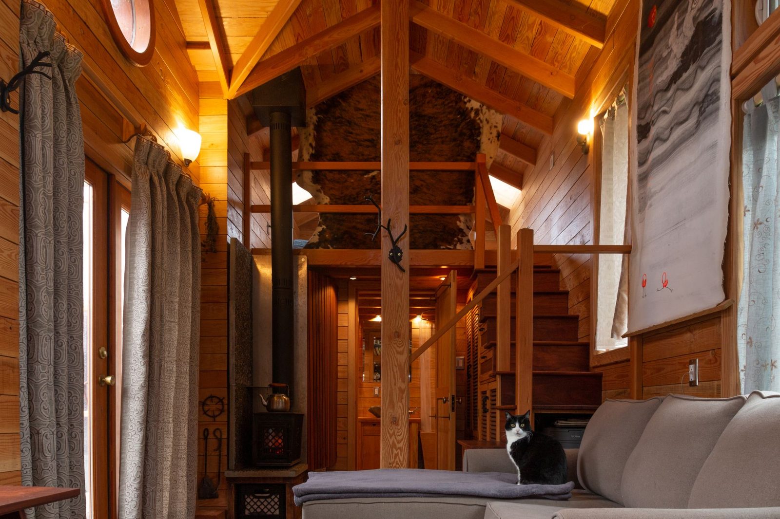 Tiny home interior with wood stove, sleeping loft, stairs and a cat on the sofa on Quadra Island