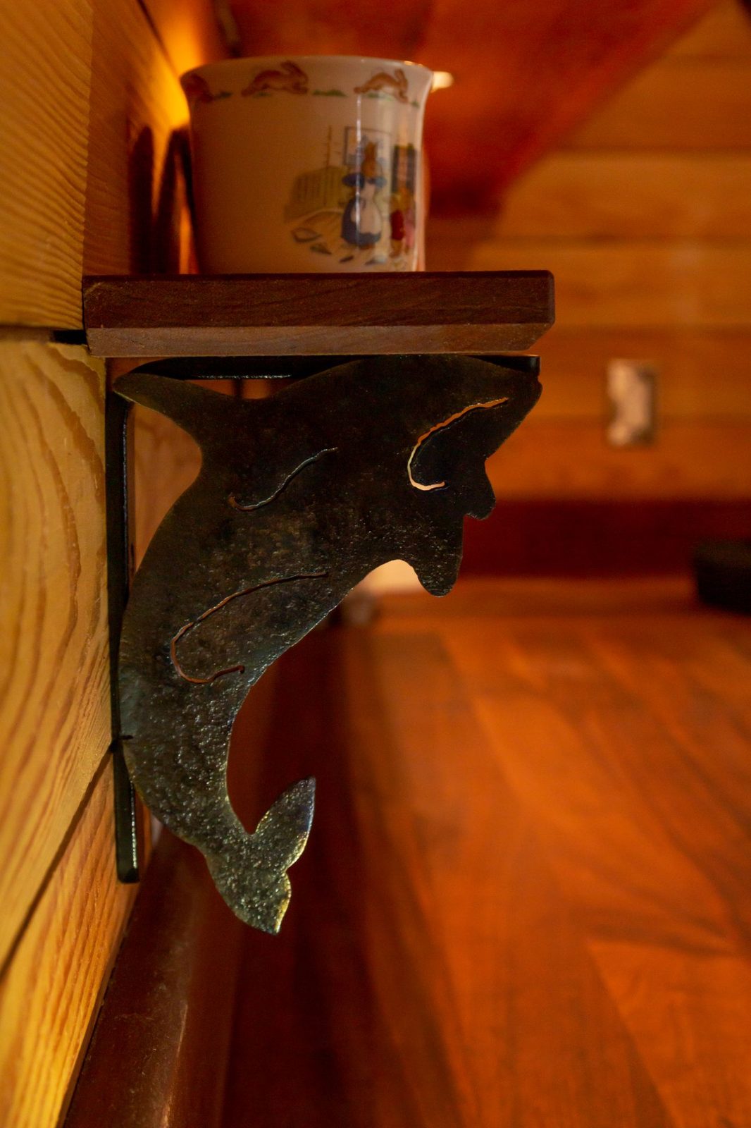 Decorative orca-shaped iron shelf bracket holding a mug in a wood-paneled tiny home