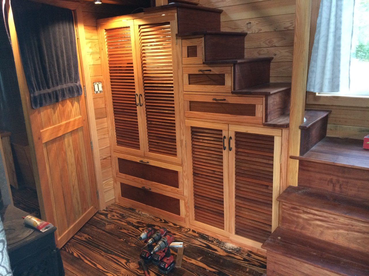 Custom storage staircase and louvered cabinets being built inside a tiny home, with tools
